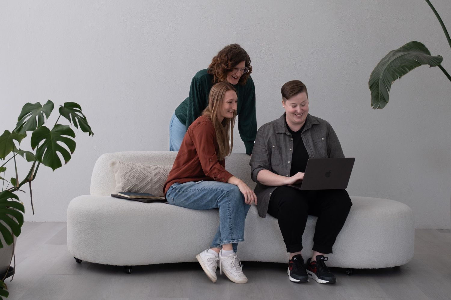 Three woman looking at a laptop, while smiling and interacting.