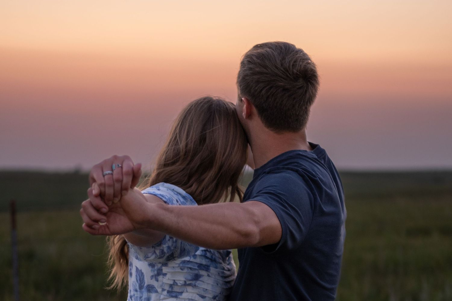 A couple outstretches their arms while they watch the sunset behind them during a couples session.