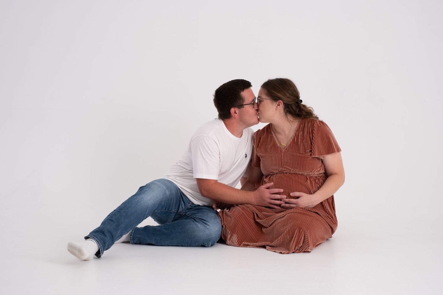 Couple sitting in front of a white infinity wall sharing an intimate moment in during maternity photoshoot.