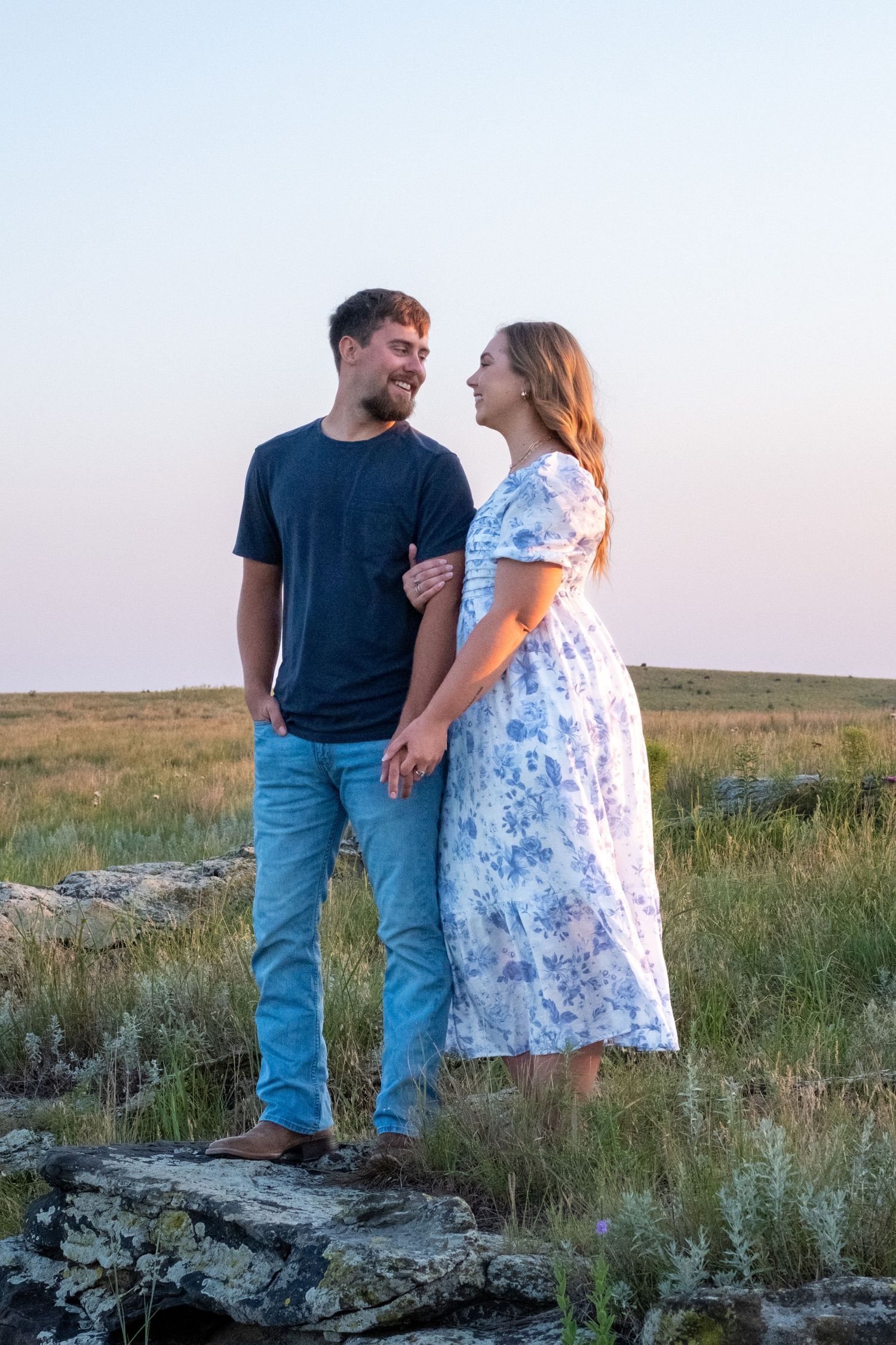 A couple look lovingly at each other while standing on a rock in a pasture in Kansas.