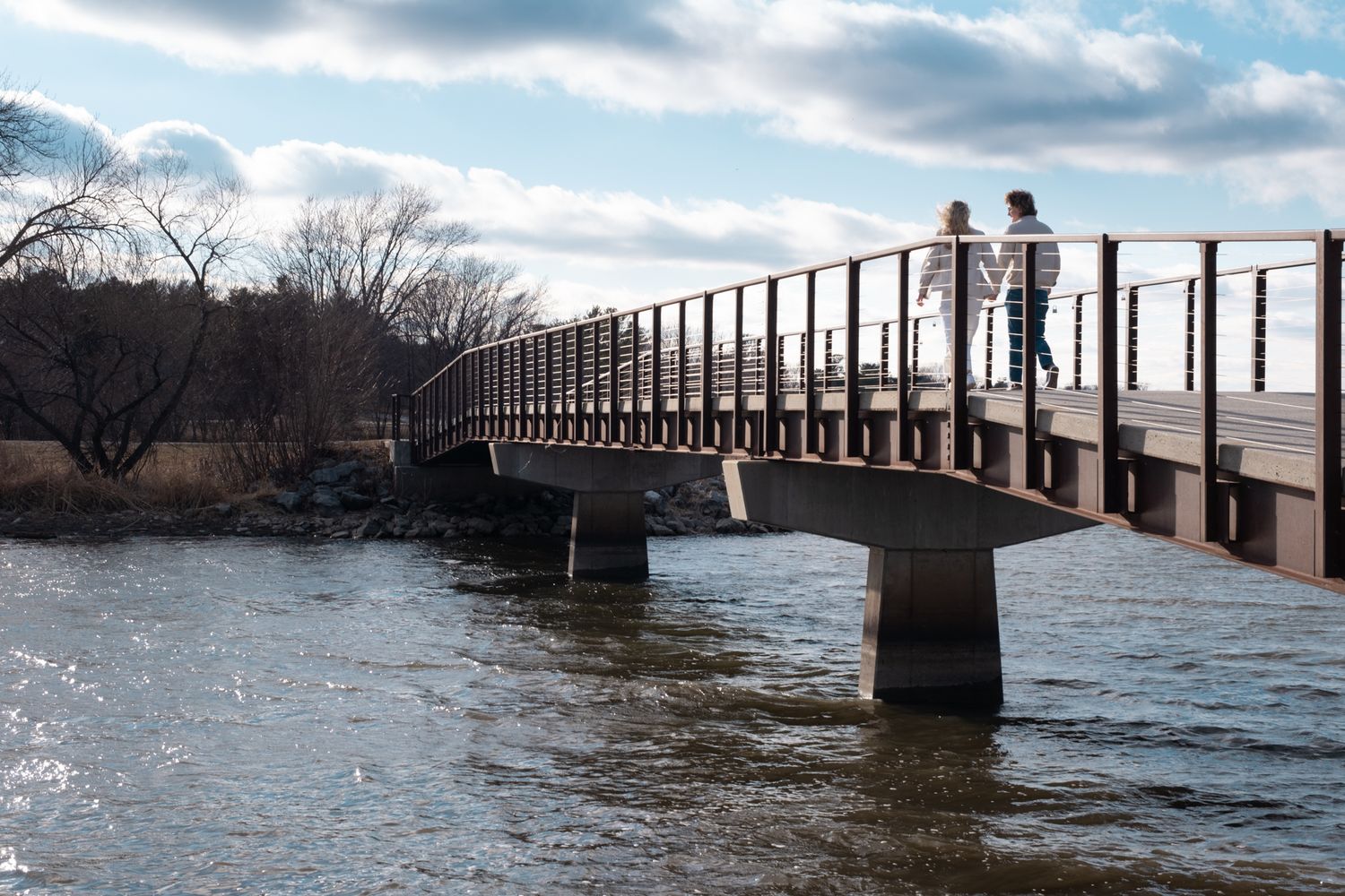 A couple is walking across a bridge over a lake.