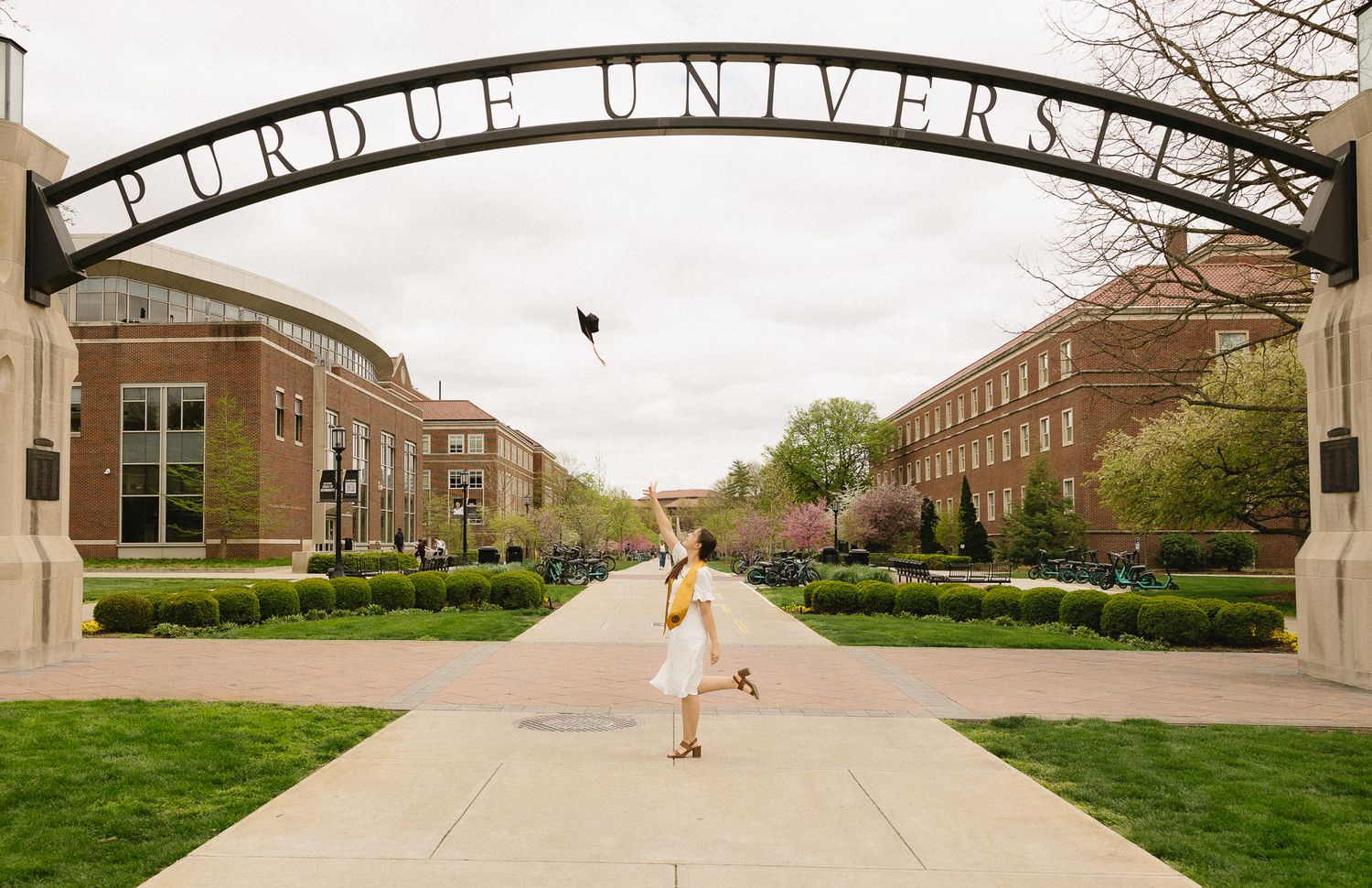 A graduate celebrates under the Purdue University entrance arch on a spring day.