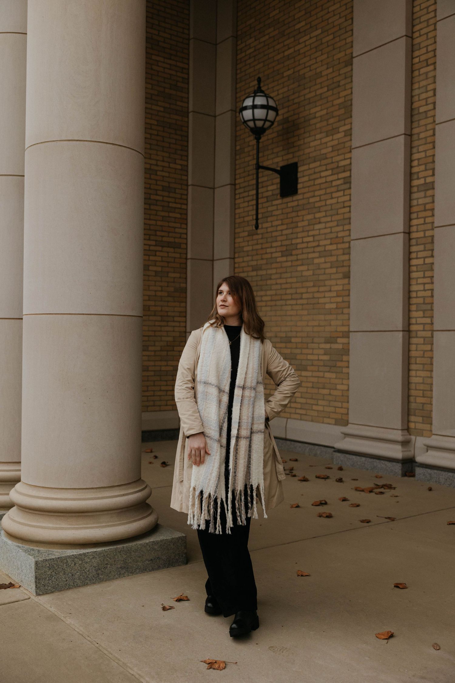 Elegant winter portrait with beige coat and scarf against columned building entrance.