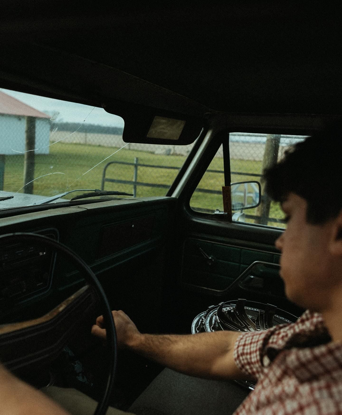 Person driving vintage car with plaid shirt on sunny day.
