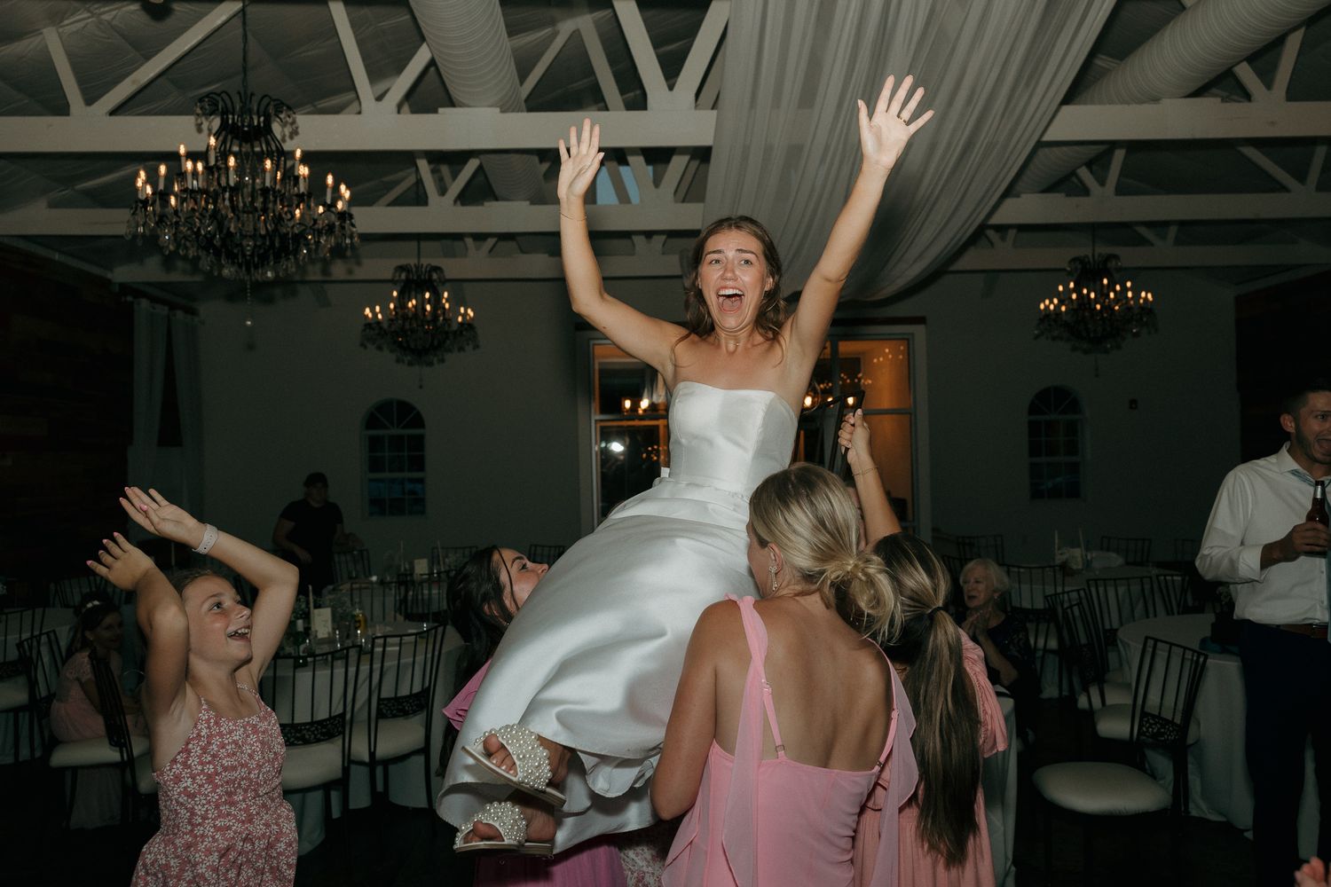 Bride dancing and jumping with joy during wedding reception in elegant venue.