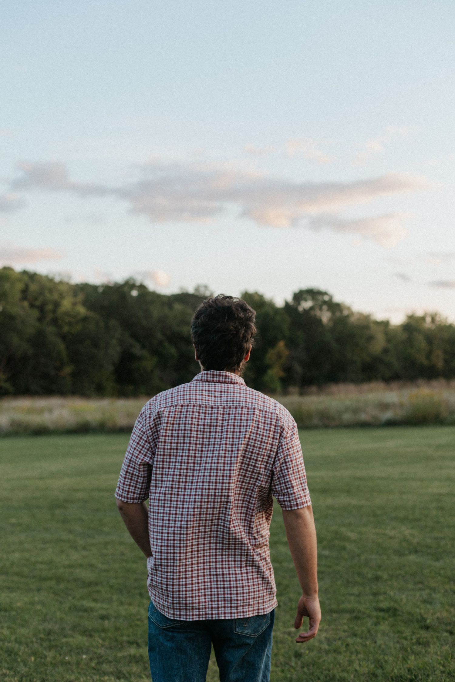 Person in plaid shirt looking out over grassy field at sunset.