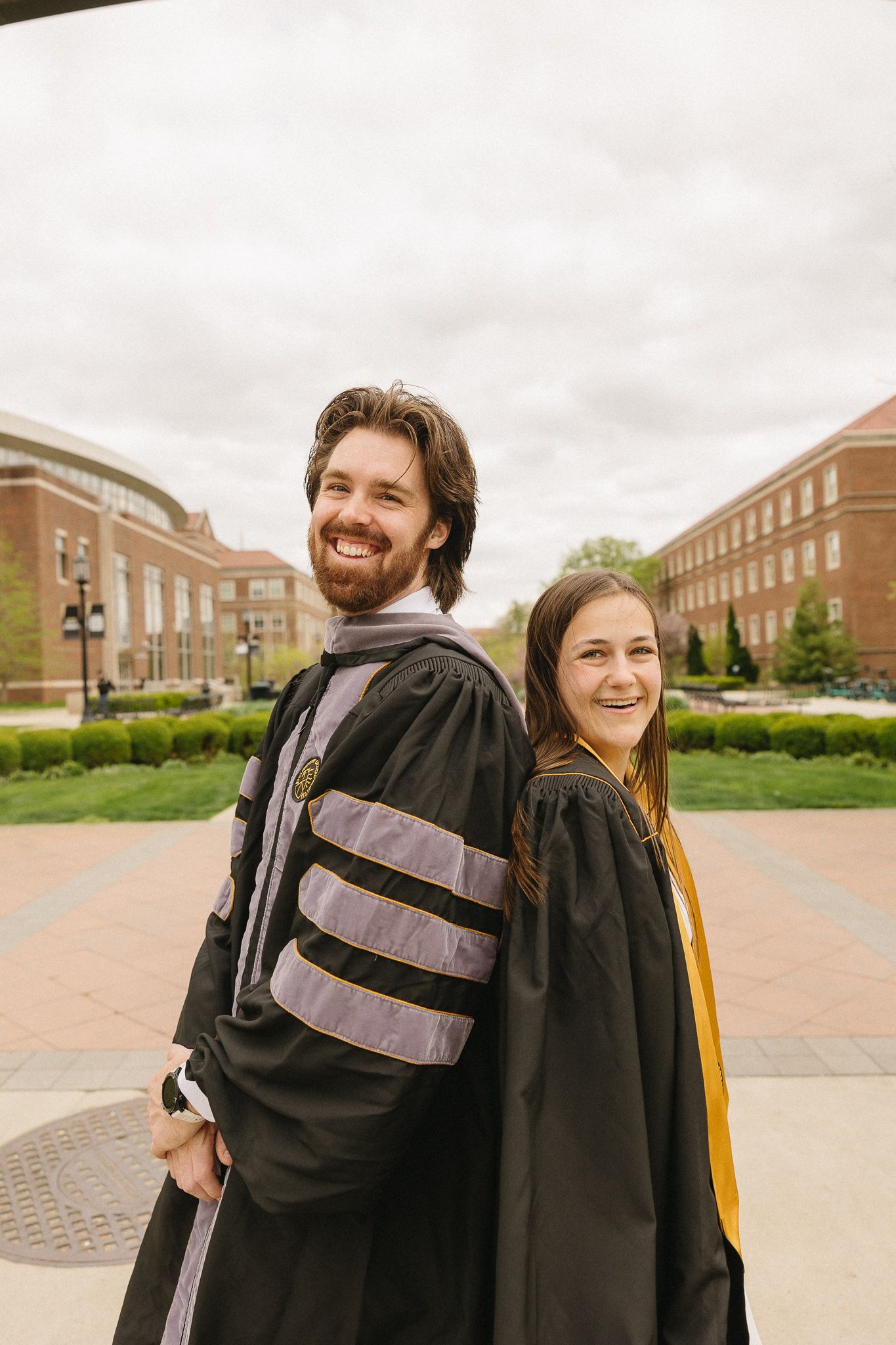 Graduates in academic regalia pose back-to-back under the Purdue University arch.