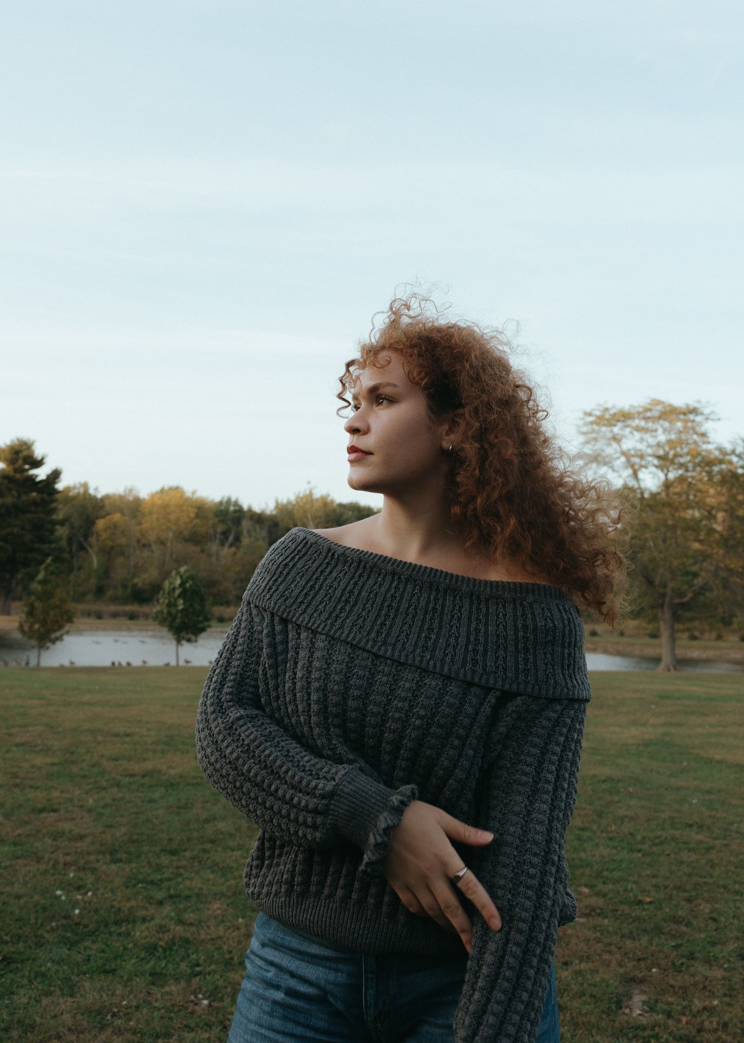 Artistic portrait of person in chunky knit sweater with natural outdoor backdrop.