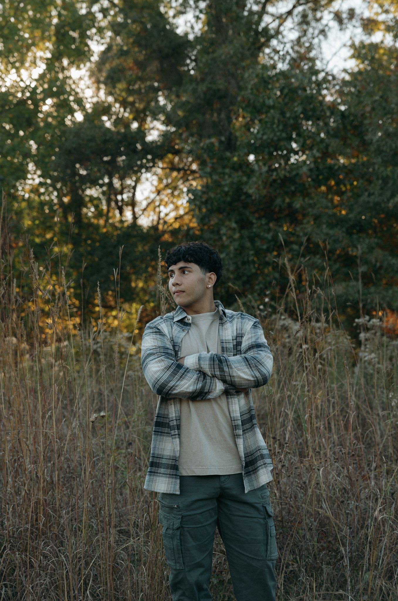 Person in plaid jacket stands among tall grass with autumn trees behind.
