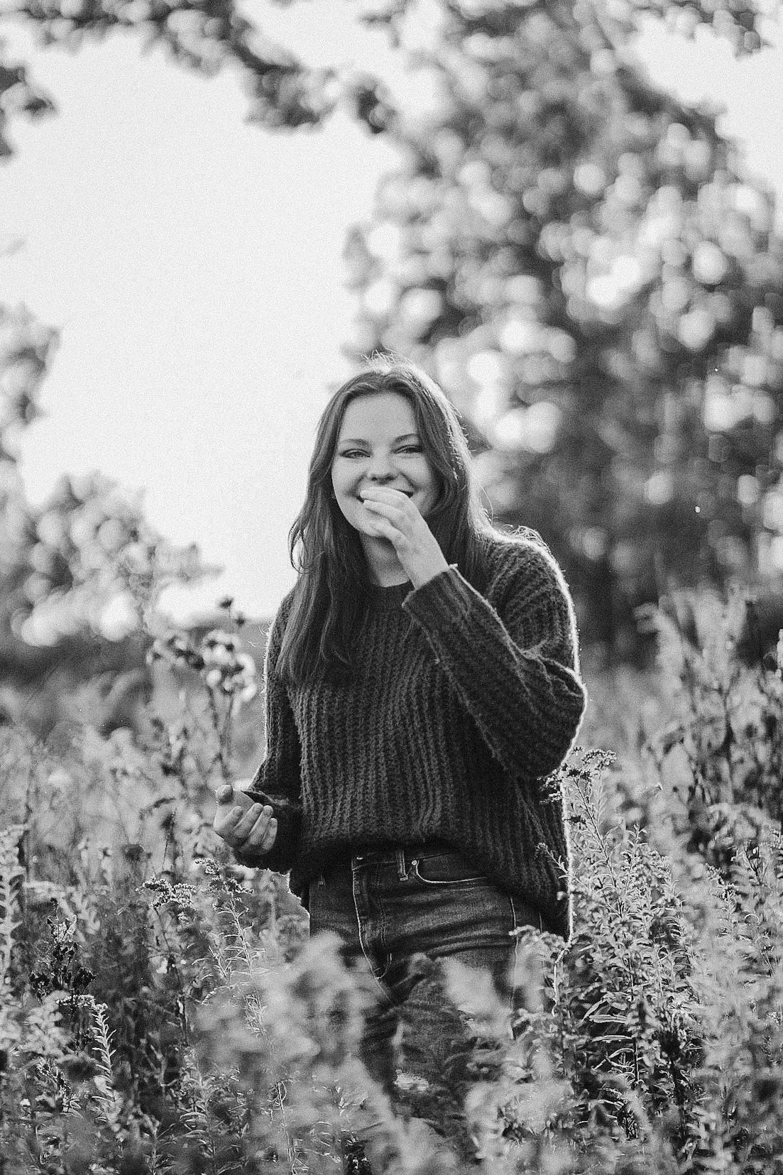 Black and white photo of someone laughing joyfully among wildflowers.
