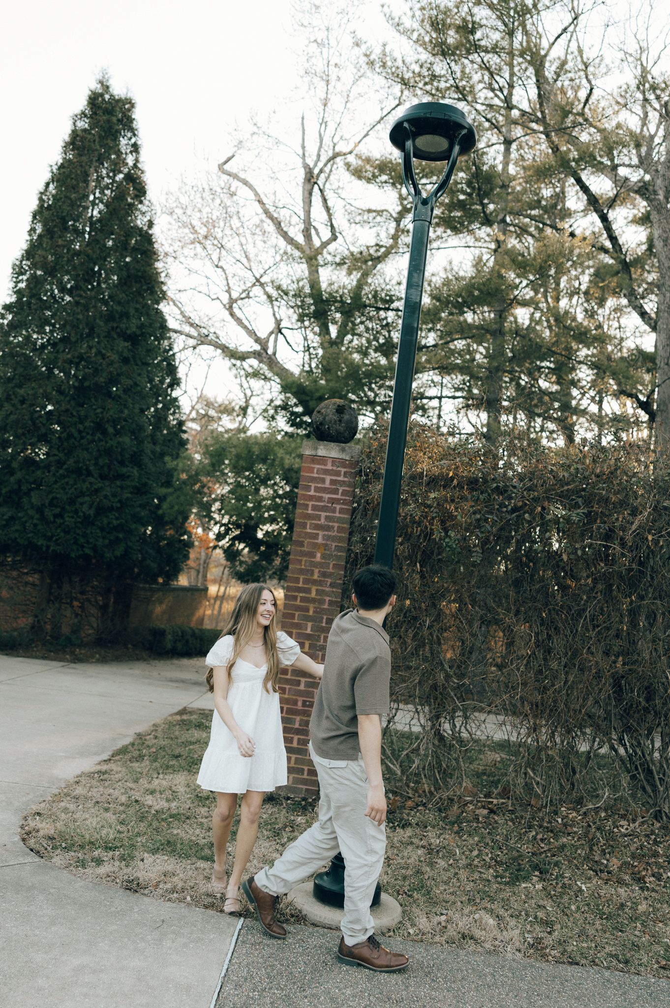 Couple walking together under vintage lamp post on brick path.