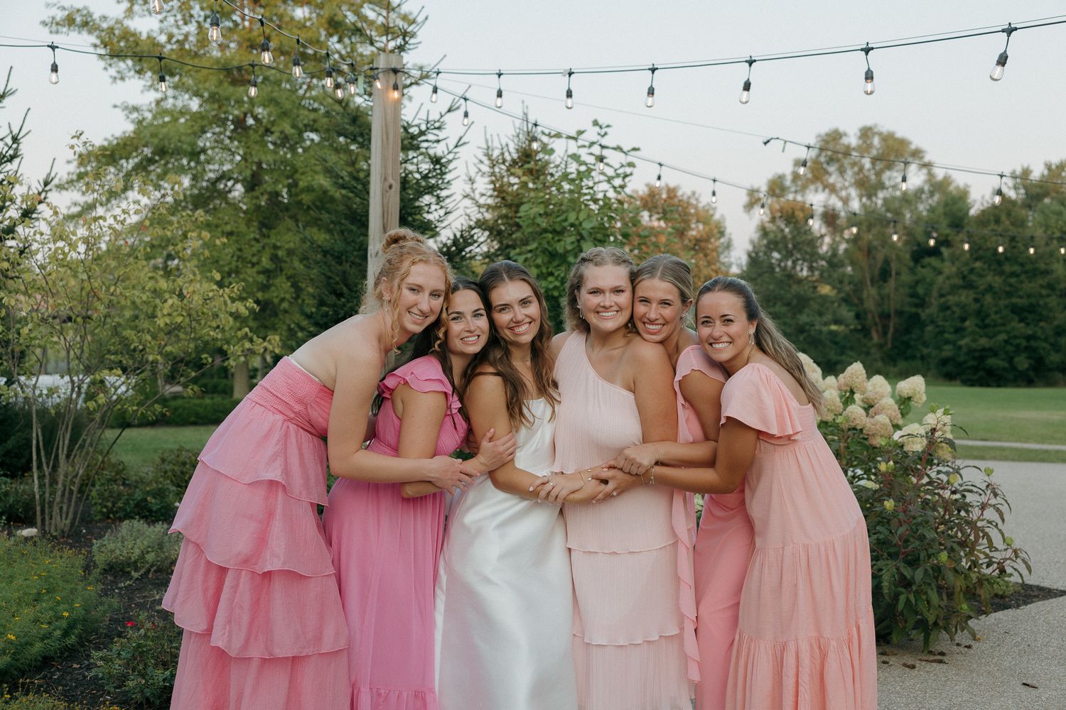 Wedding party in pink dresses hugging and posing together outdoors.