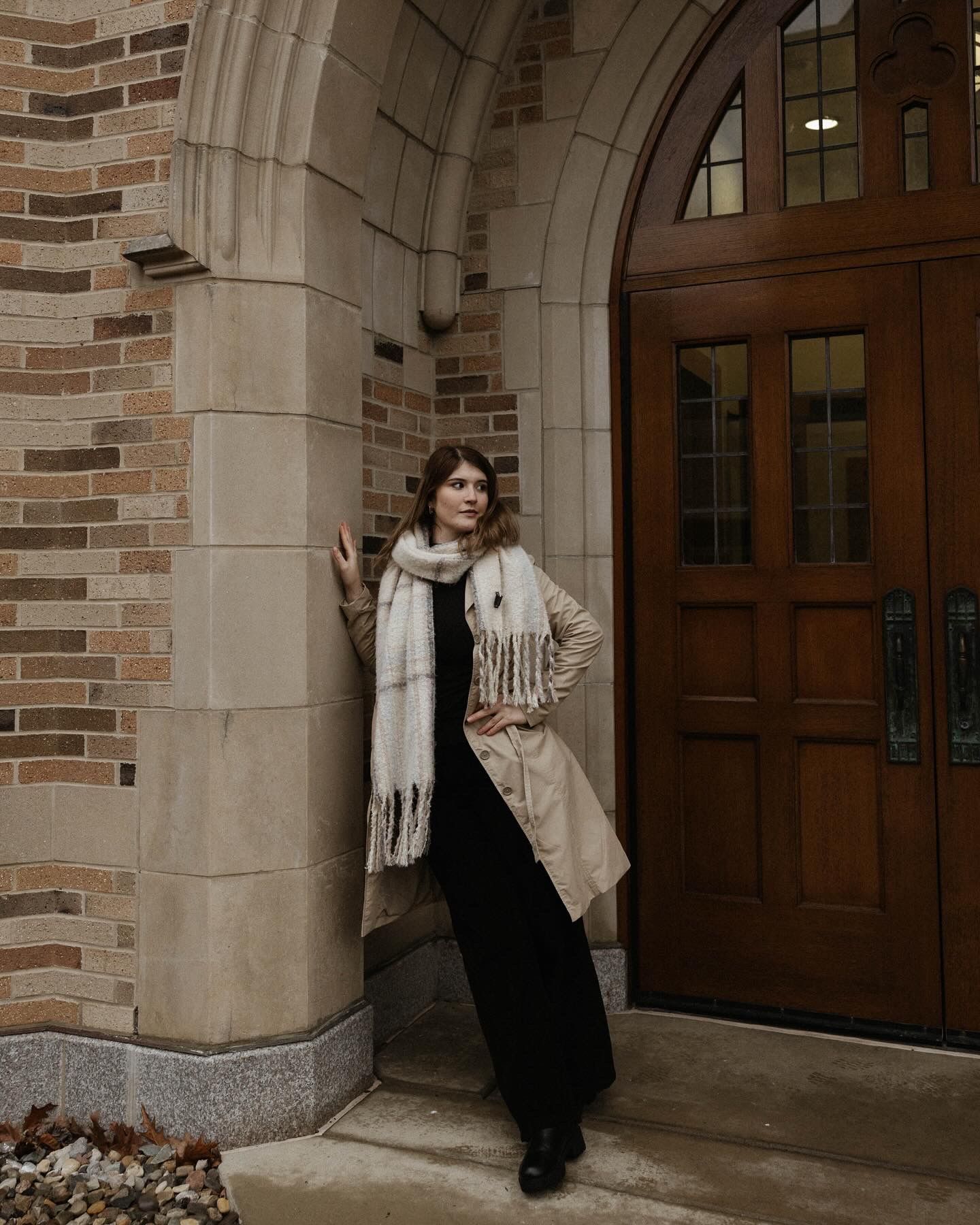 Stylish winter fashion portrait under classic stone archway with wooden doors.