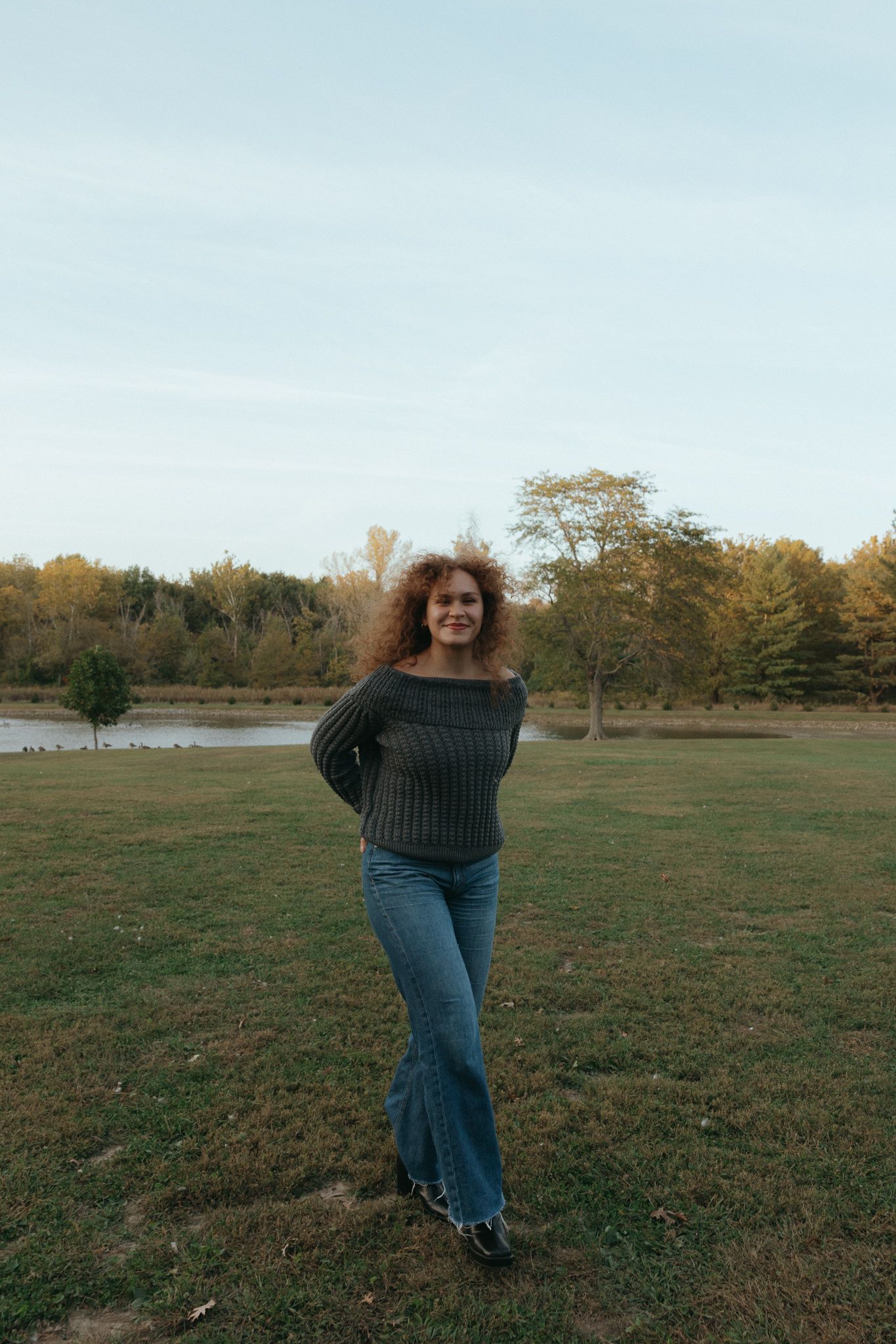 Casual outdoor portrait in gray sweater and jeans against autumn landscape.