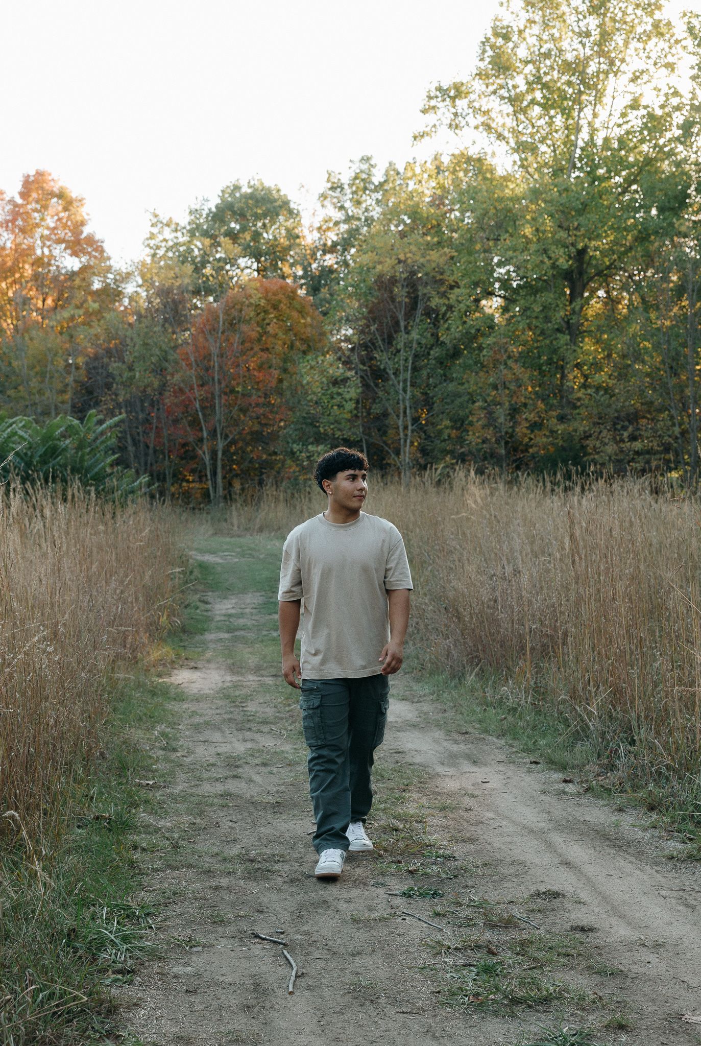 Person walking along a dirt path through tall grass and autumn trees.