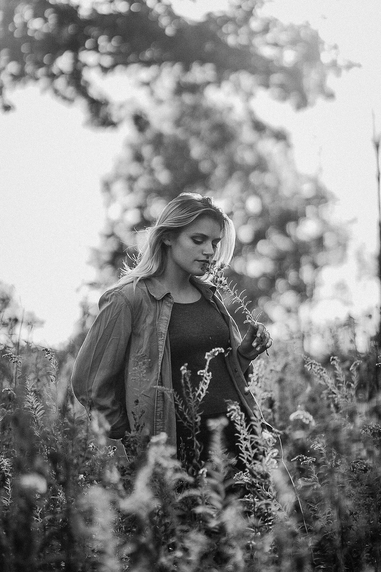 Moody black and white portrait of a person standing in a wildflower field wearing a jacket.