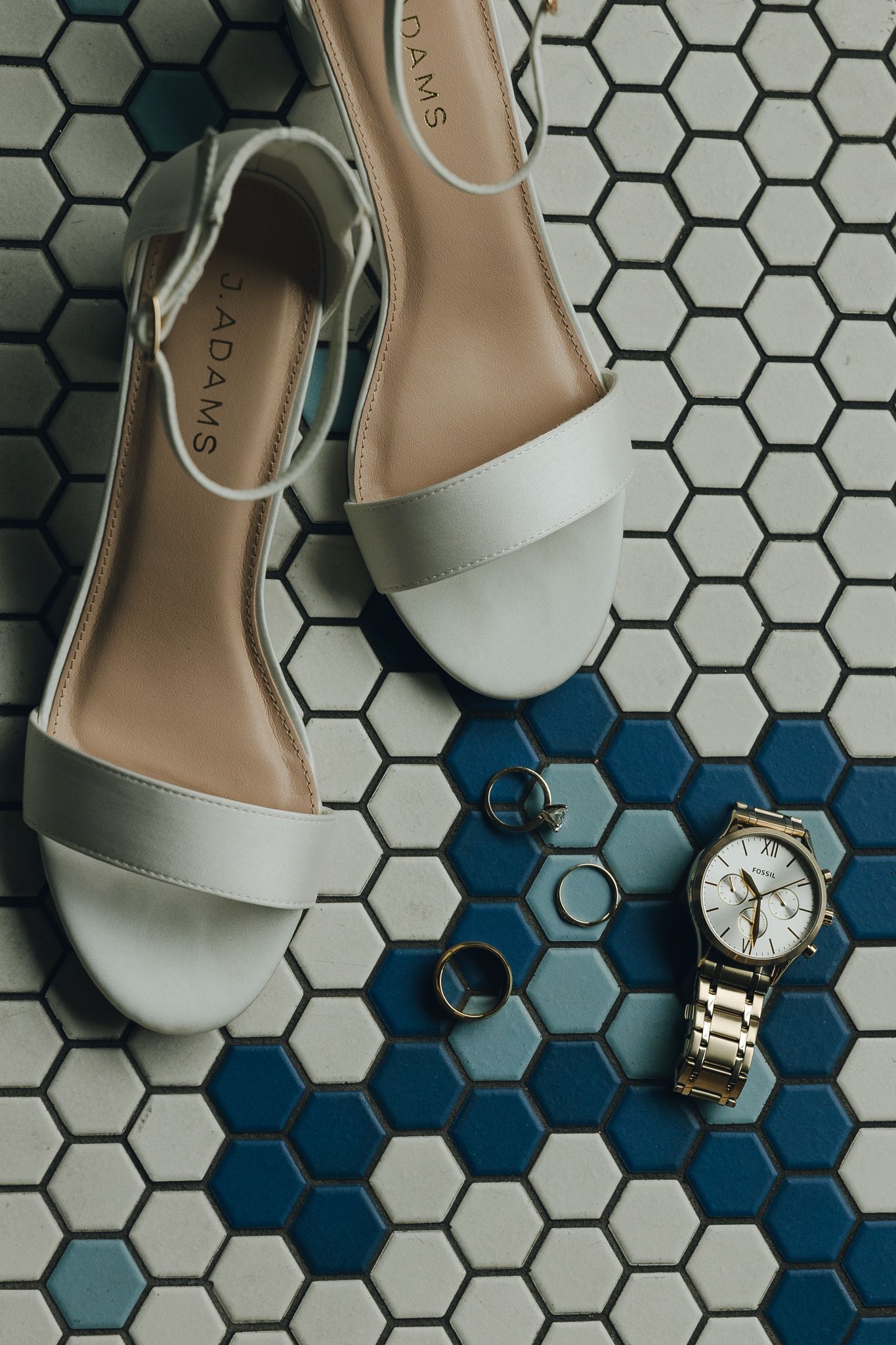 White sandals, rings and silver watch arranged on hexagonal tile pattern.