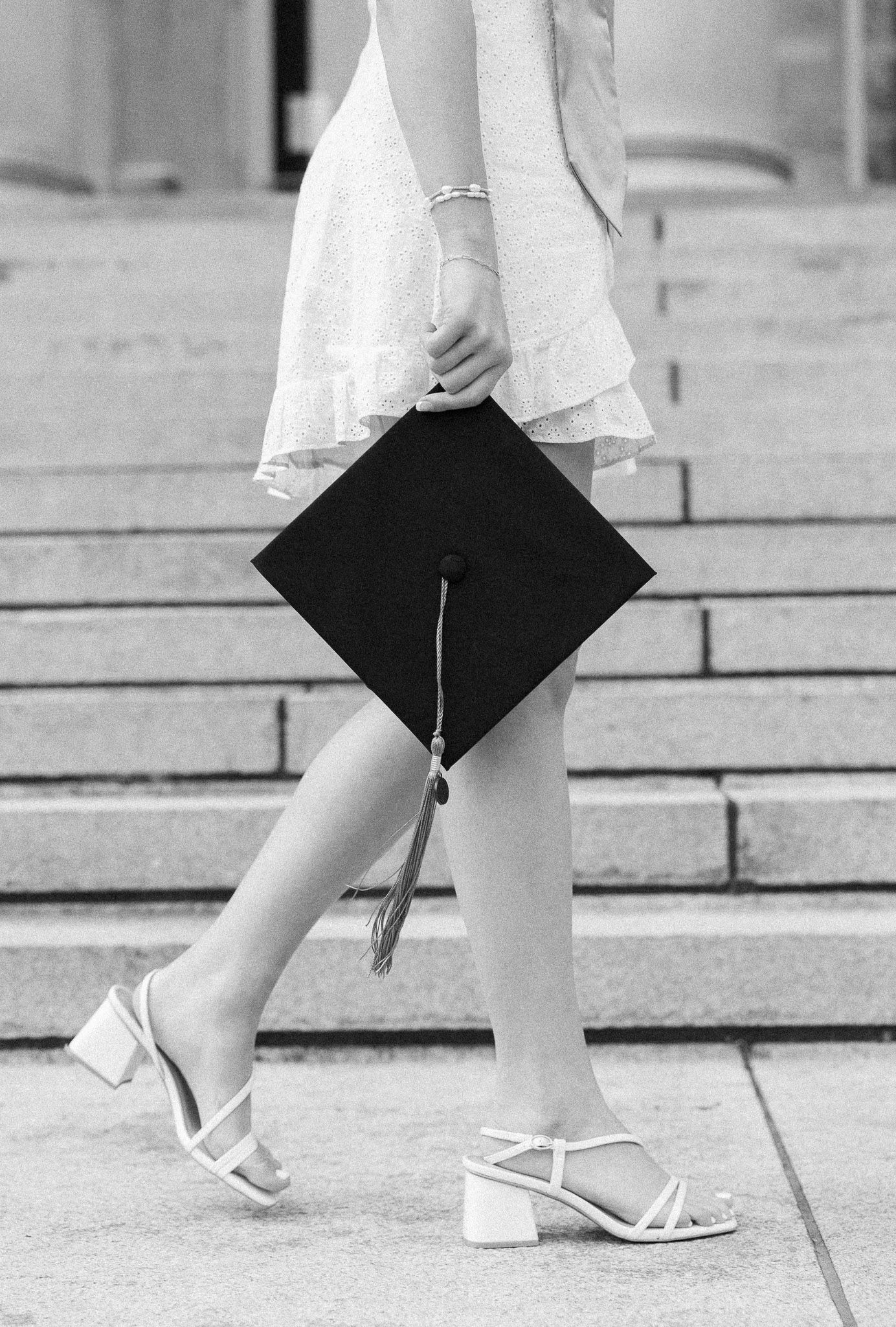 Black and white photo of graduate holding cap while walking down stone steps.