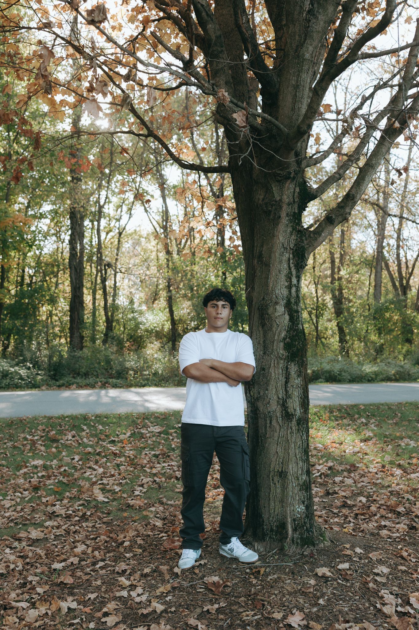 Person standing against large tree trunk in casual attire during fall season.