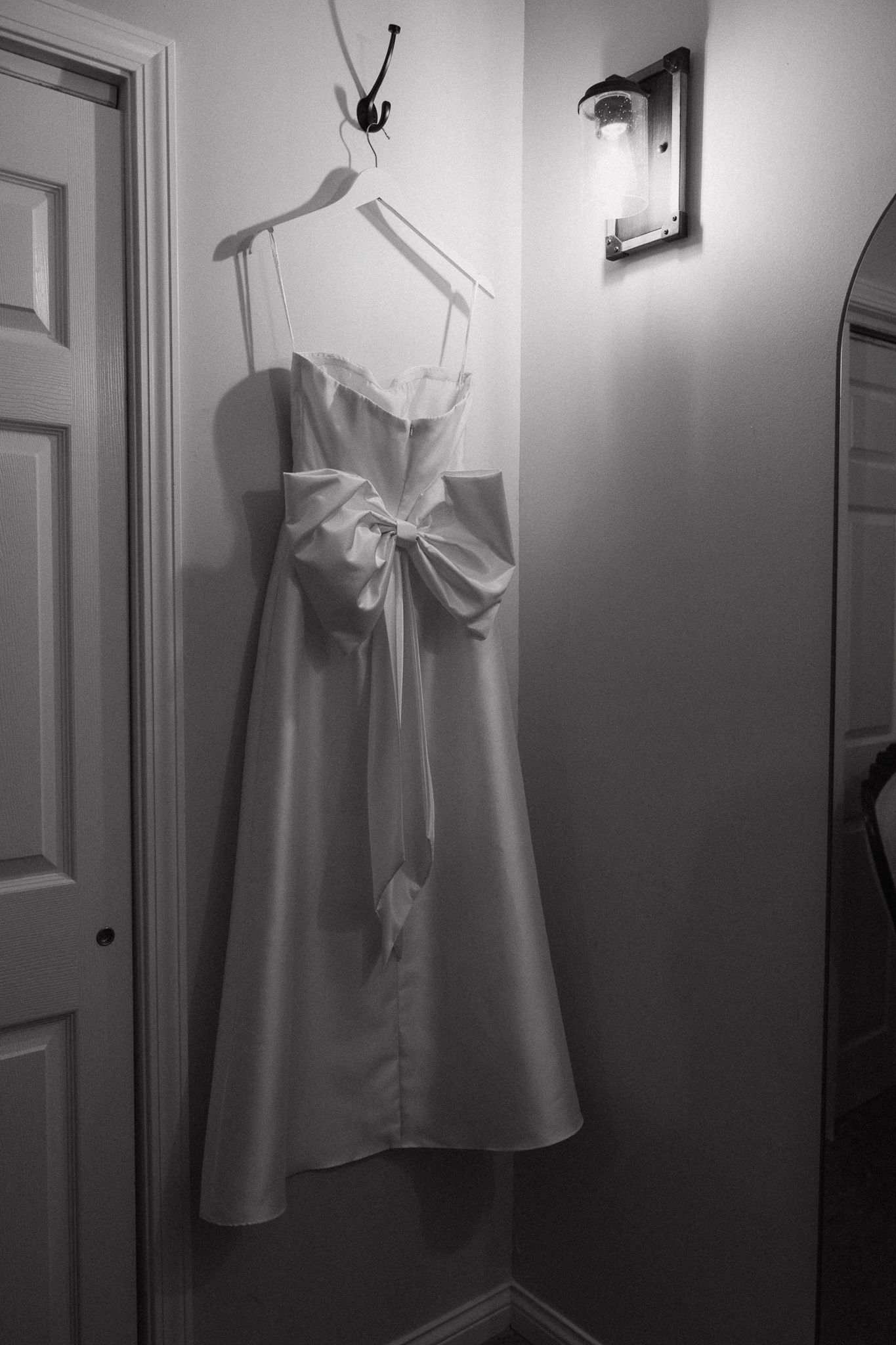 Elegant white wedding dress with bow detail hanging on display in corner.