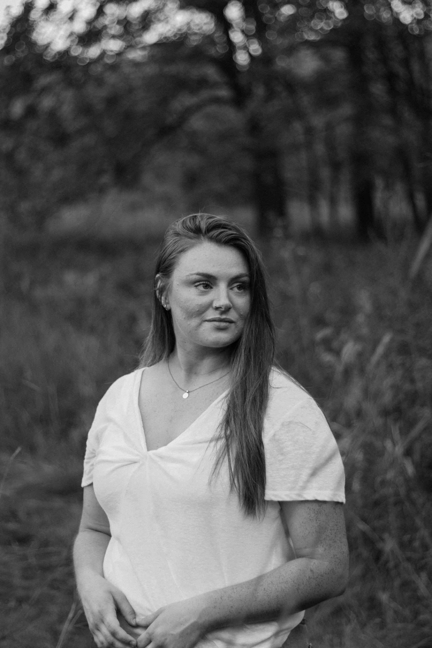 Casual black and white portrait of someone in a white t-shirt against a natural outdoor background.