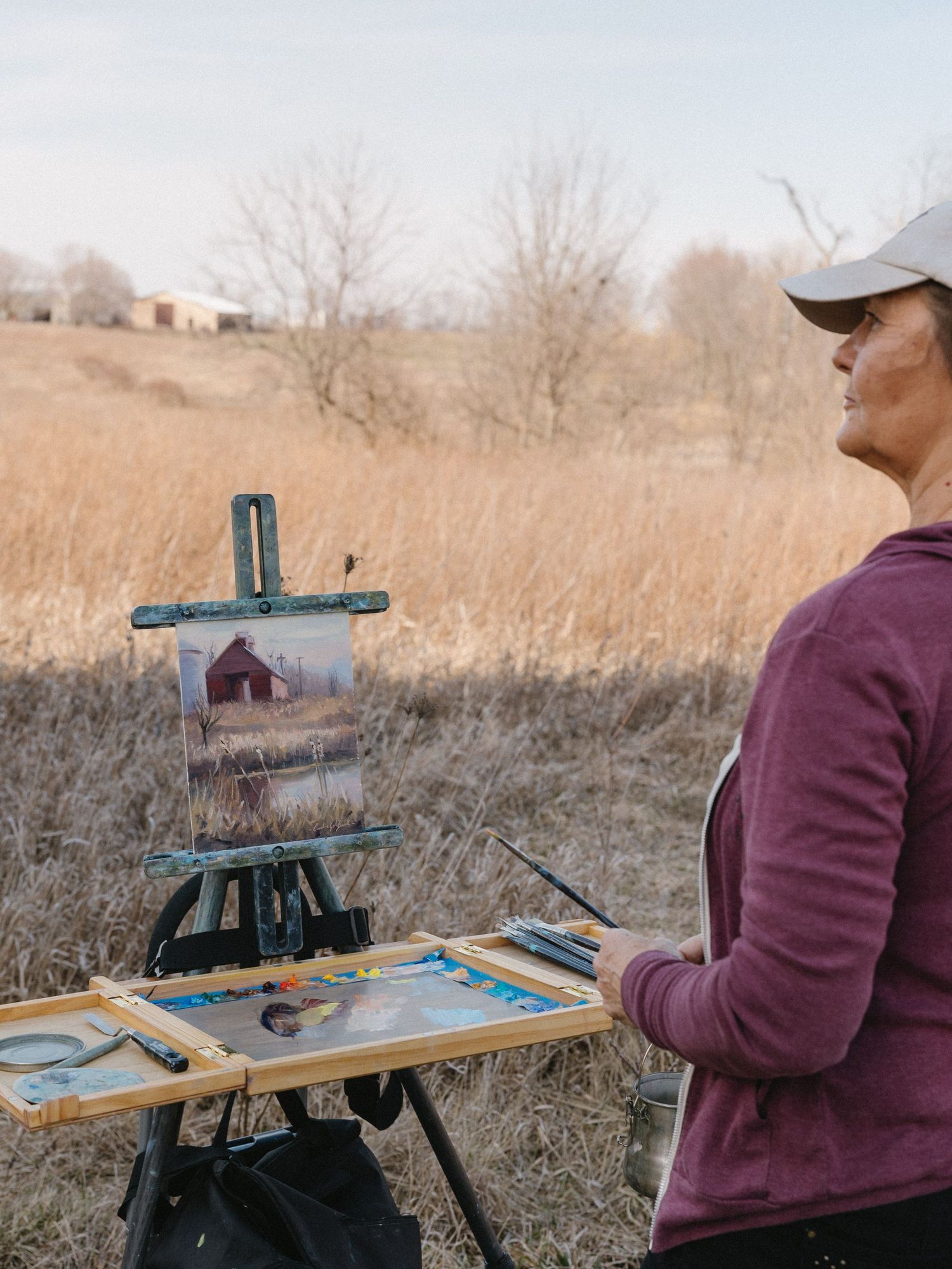 Artist painting a rustic barn scene on location in a rural field during autumn.