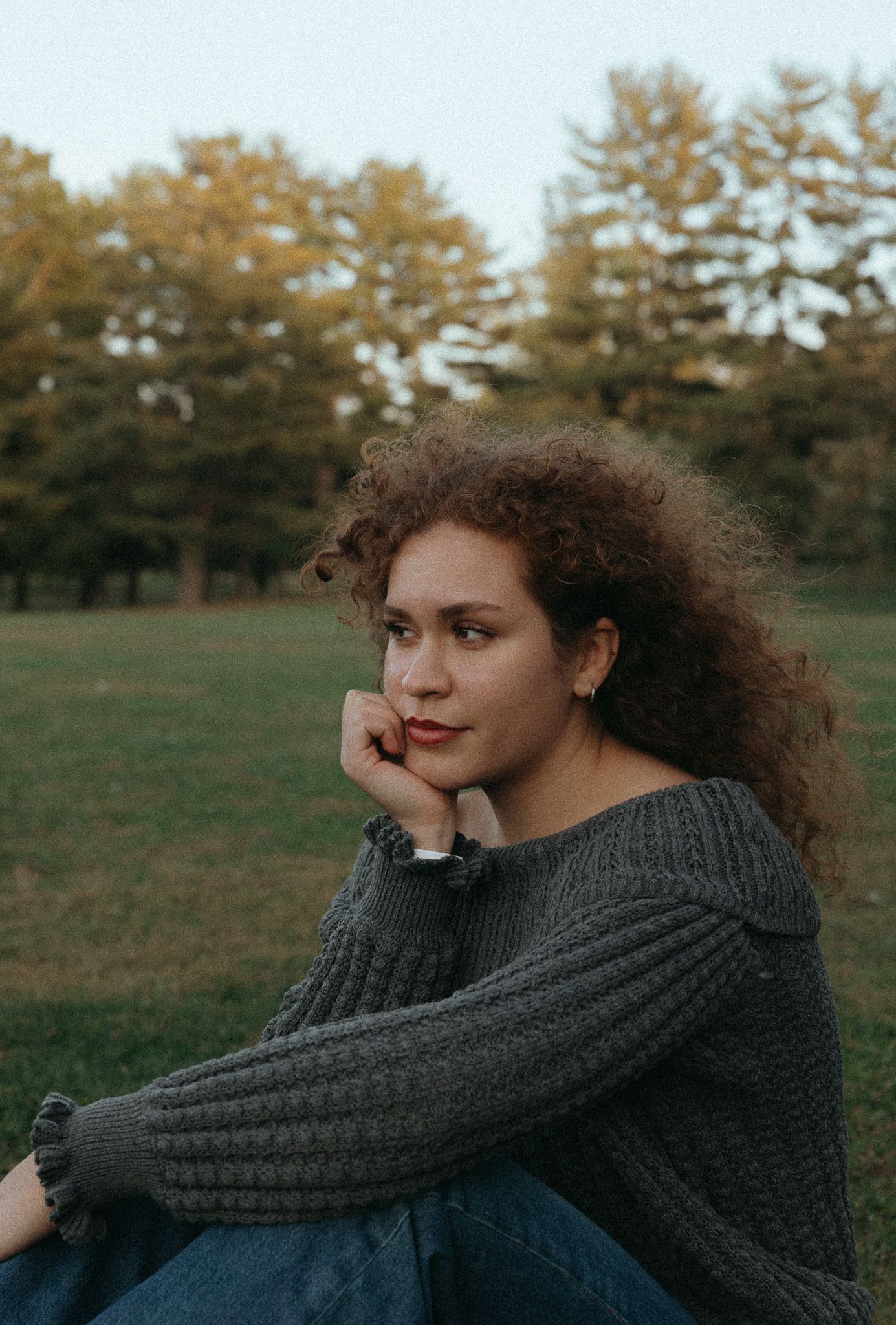 Thoughtful portrait against autumn trees wearing gray knit sweater.