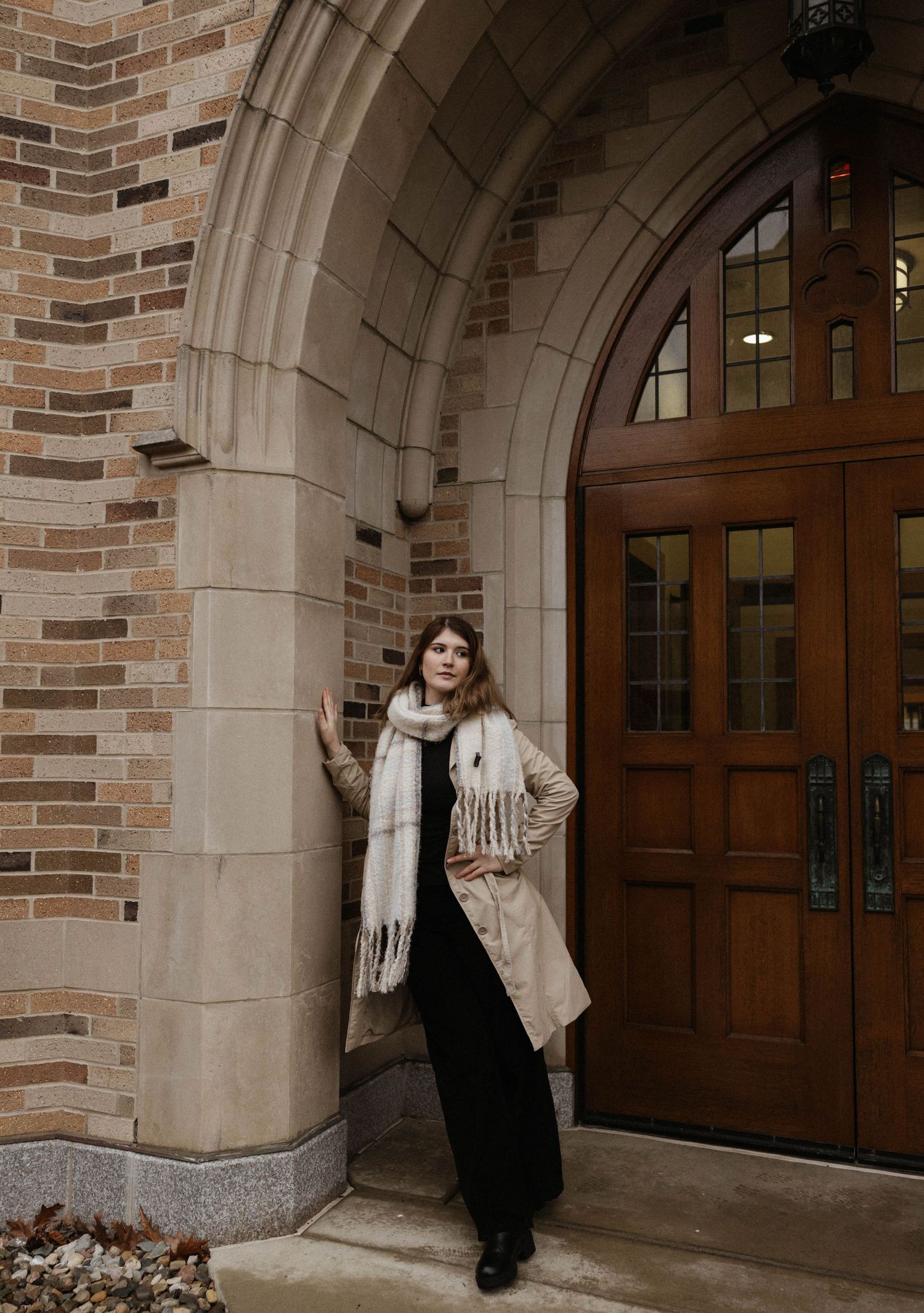 Fashion portrait featuring cream coat and scarf against brick and stone architecture.
