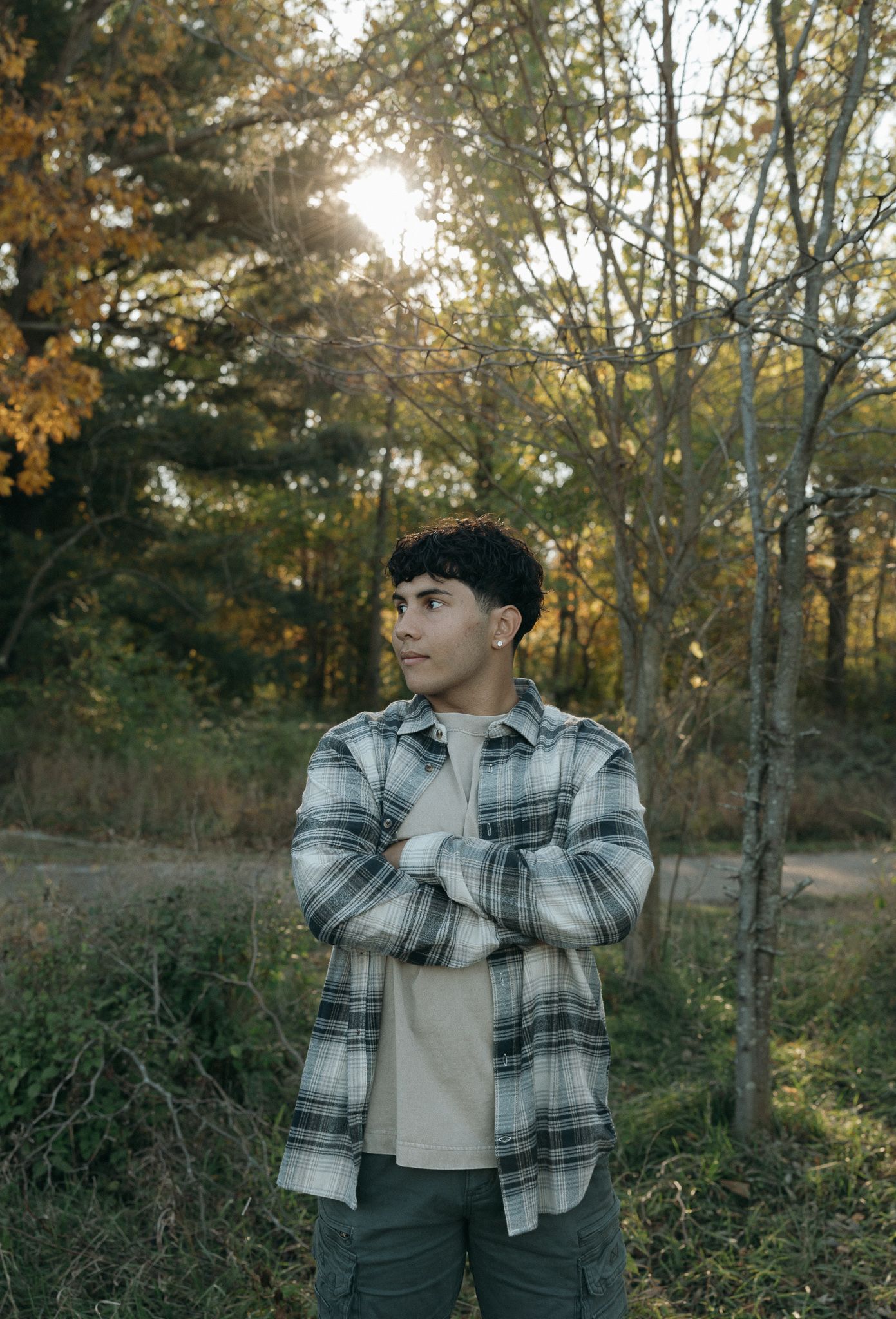 Person in plaid flannel jacket poses against autumn foliage at sunset.
