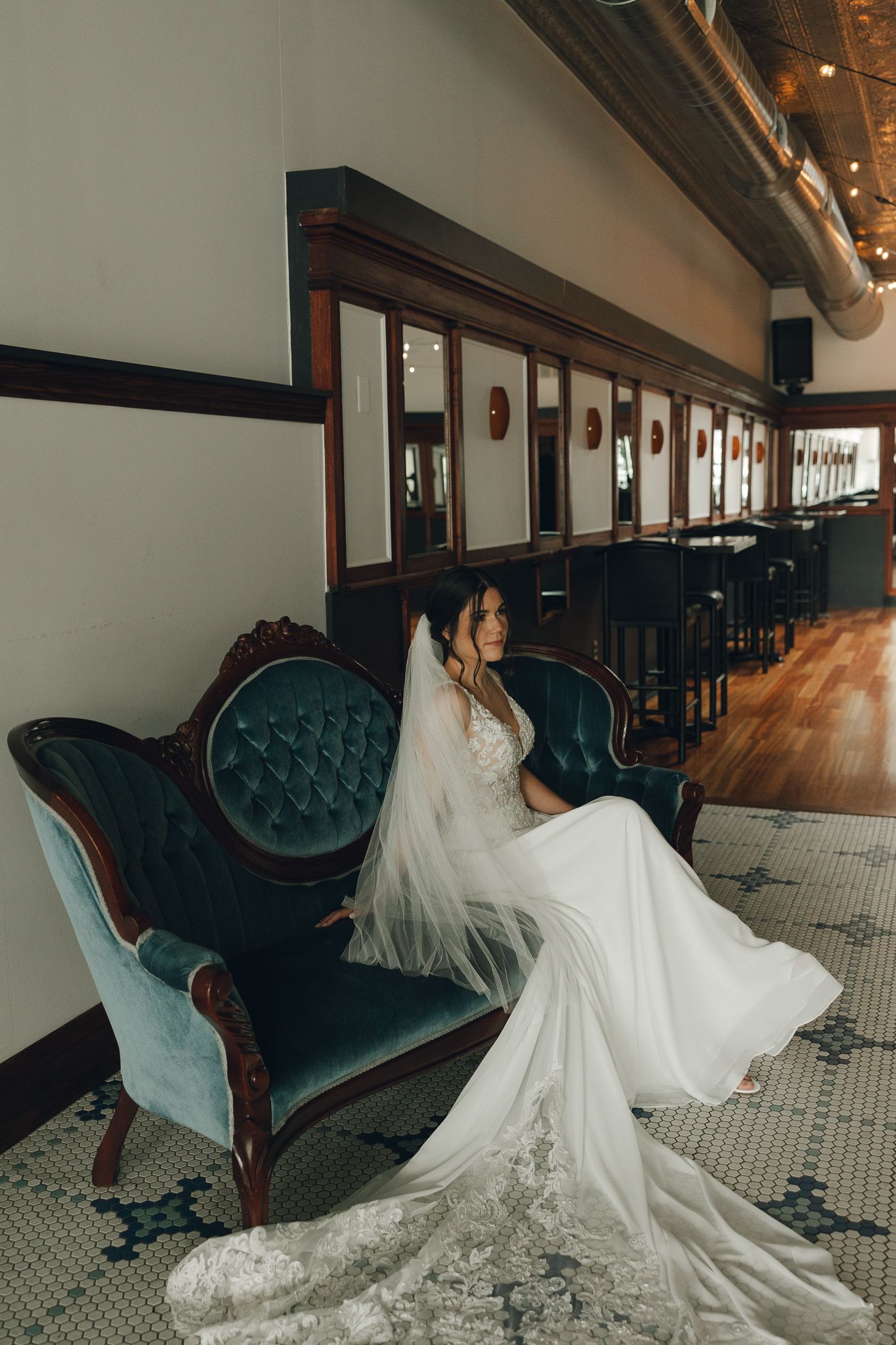 Bride in flowing lace gown resting on teal vintage velvet couch.