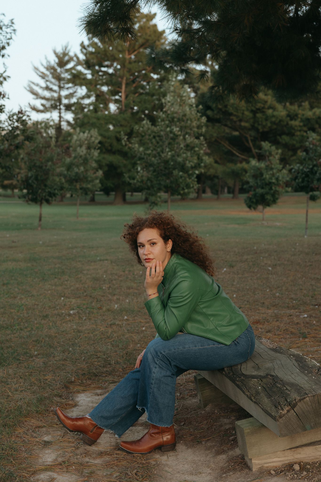 Person in green sweater sitting thoughtfully on wooden bench in park setting.