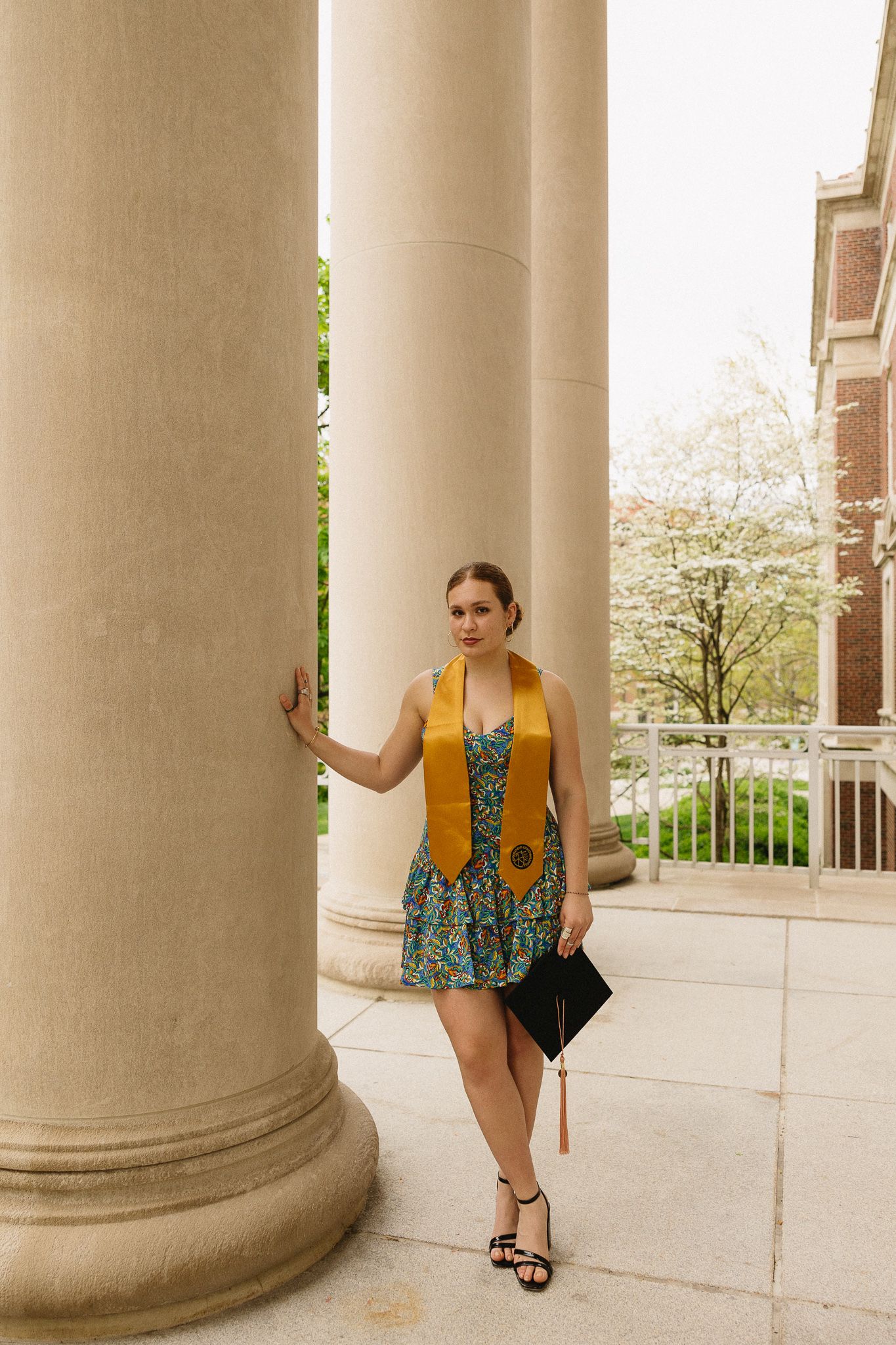 Graduate in yellow stole and floral dress posing by classical column.