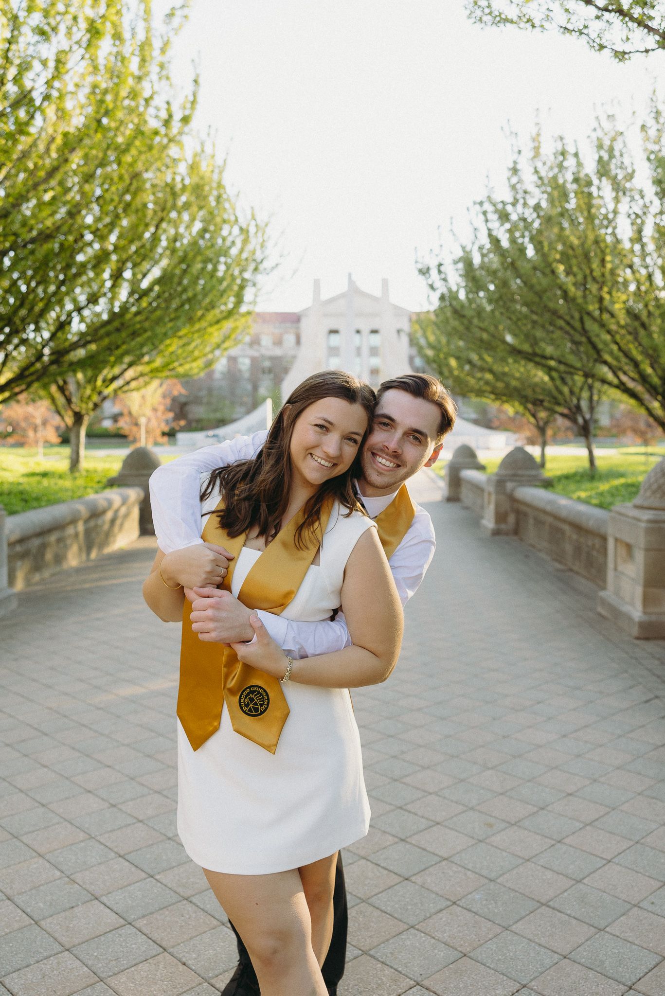 Graduation celebration photo on campus walkway with trees and building in background.