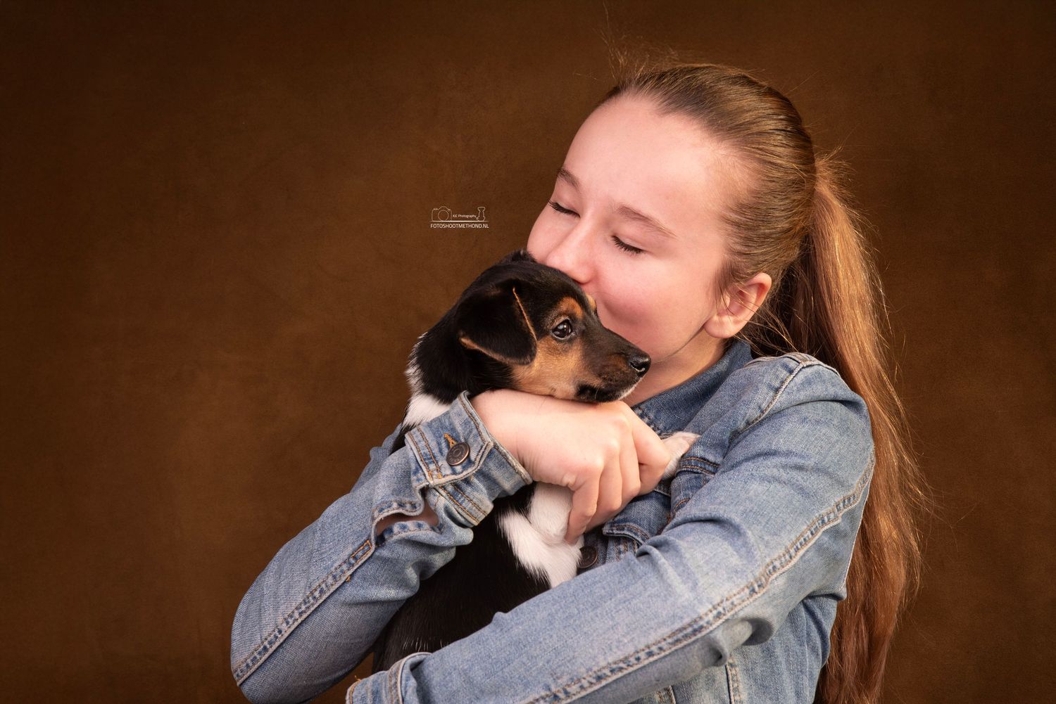 Knuffelmoment tijdens fotoshoot met puppy en kind tegen een leren achtergrond in Doetinchem