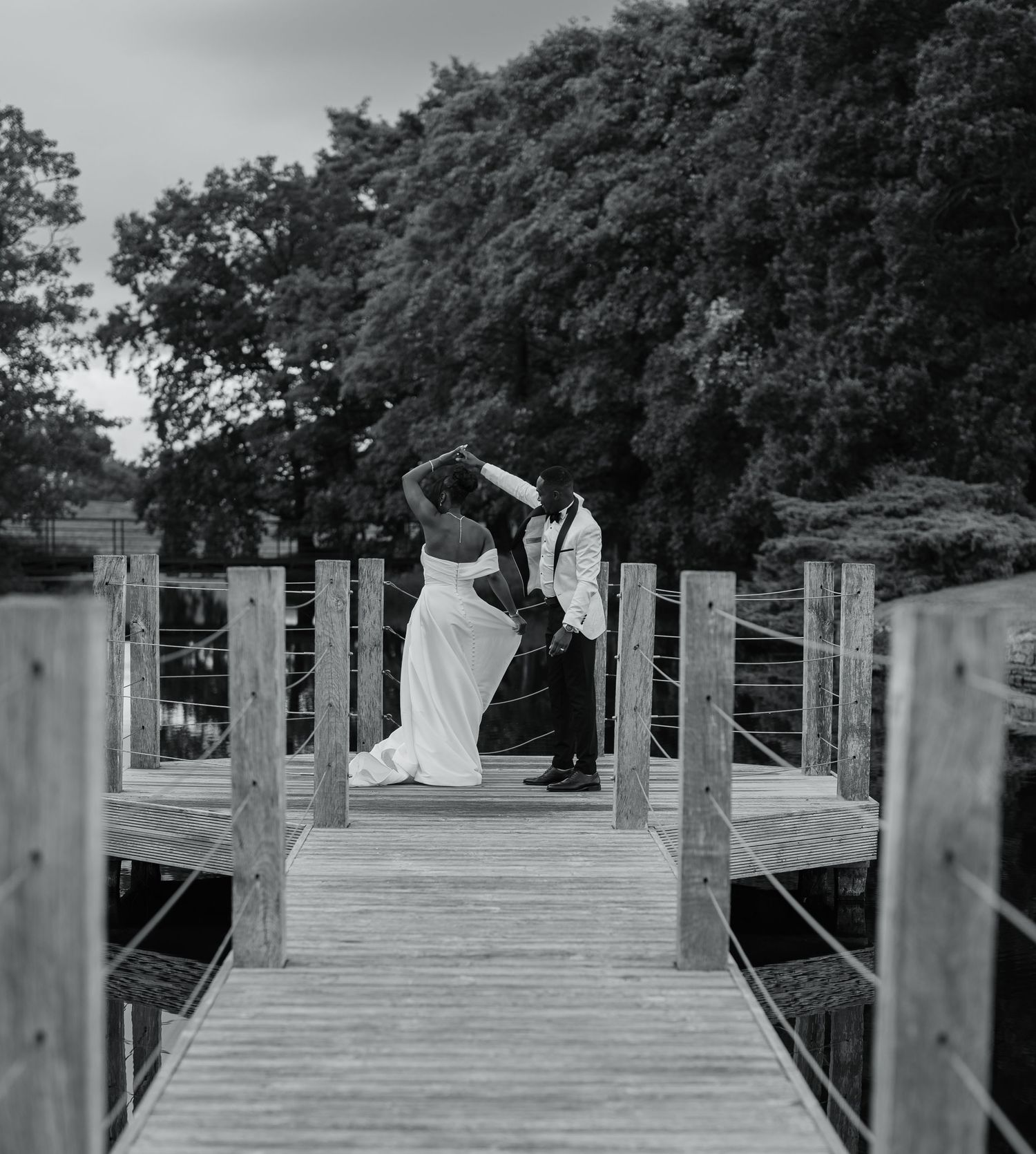 A wooden dock stretches out over a serene lake surrounded by lush trees on a beautiful day.