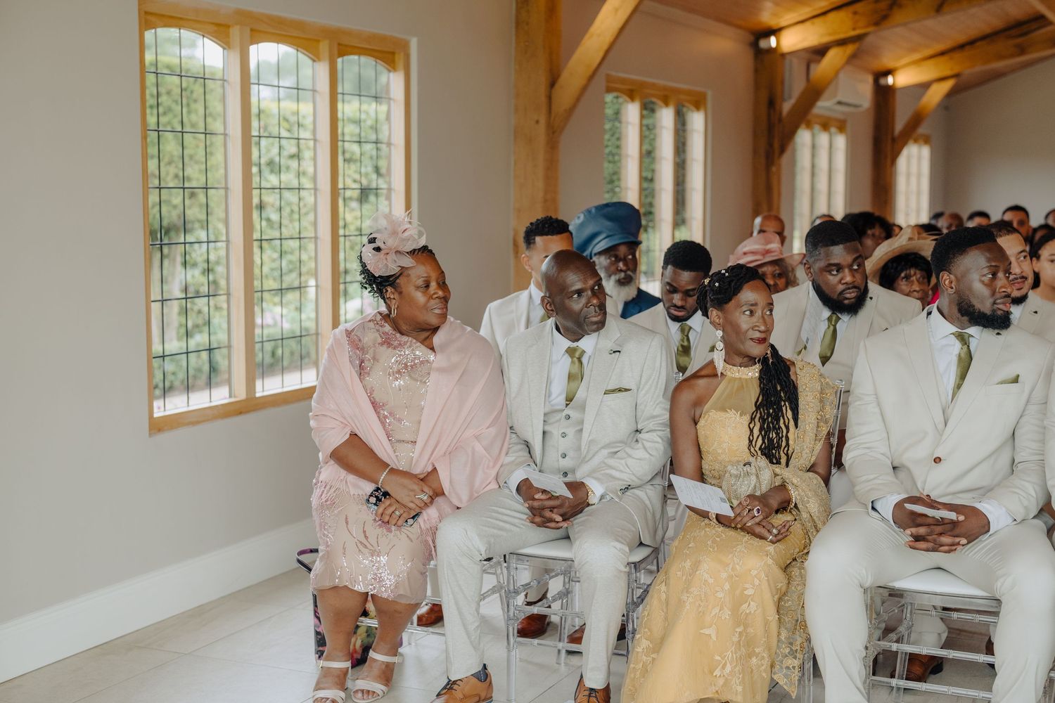 Wedding guests seated in rows during ceremony in bright venue with wooden beams and windows.