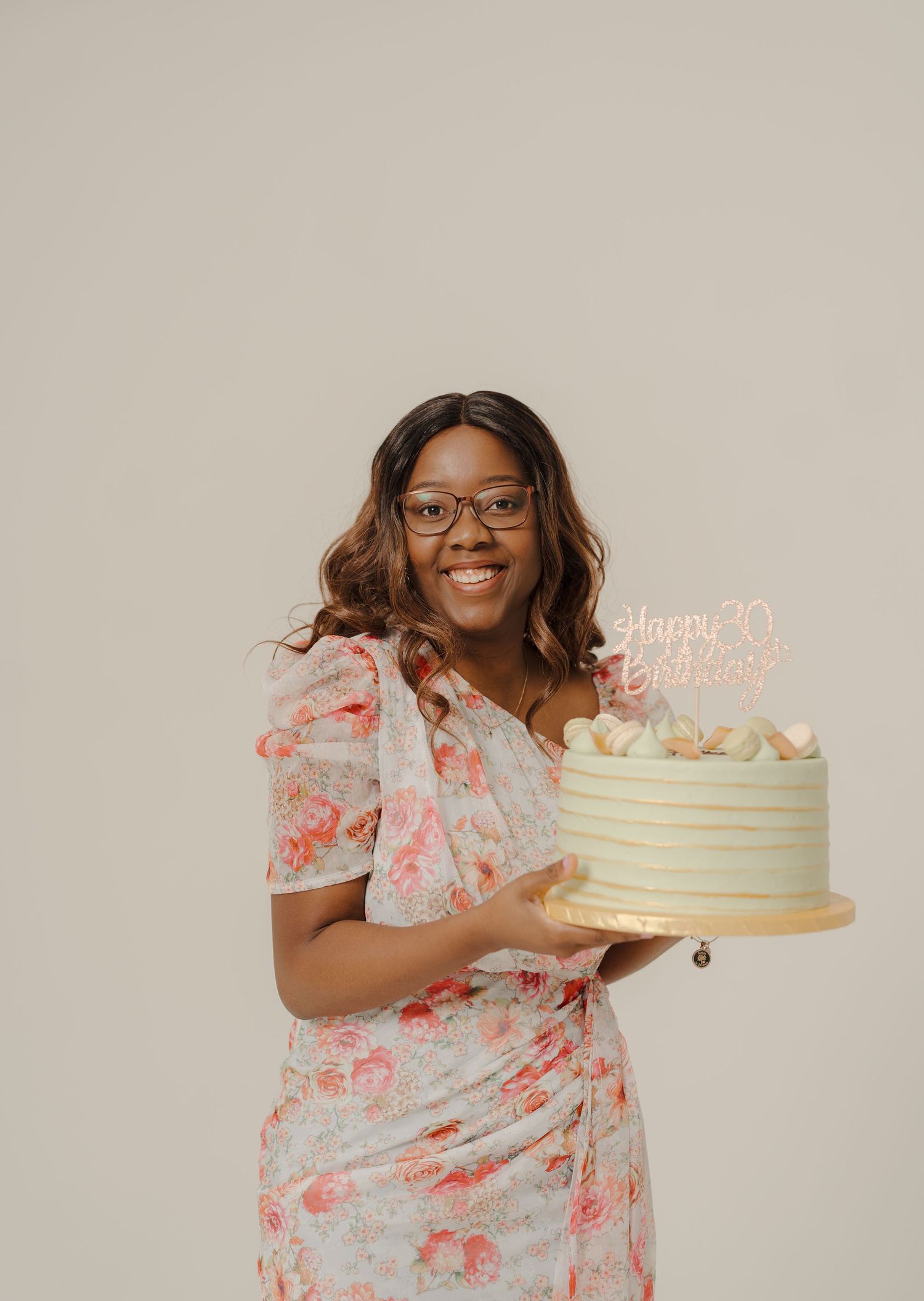 Person in floral dress celebrates with a beautiful cream-colored birthday cake.