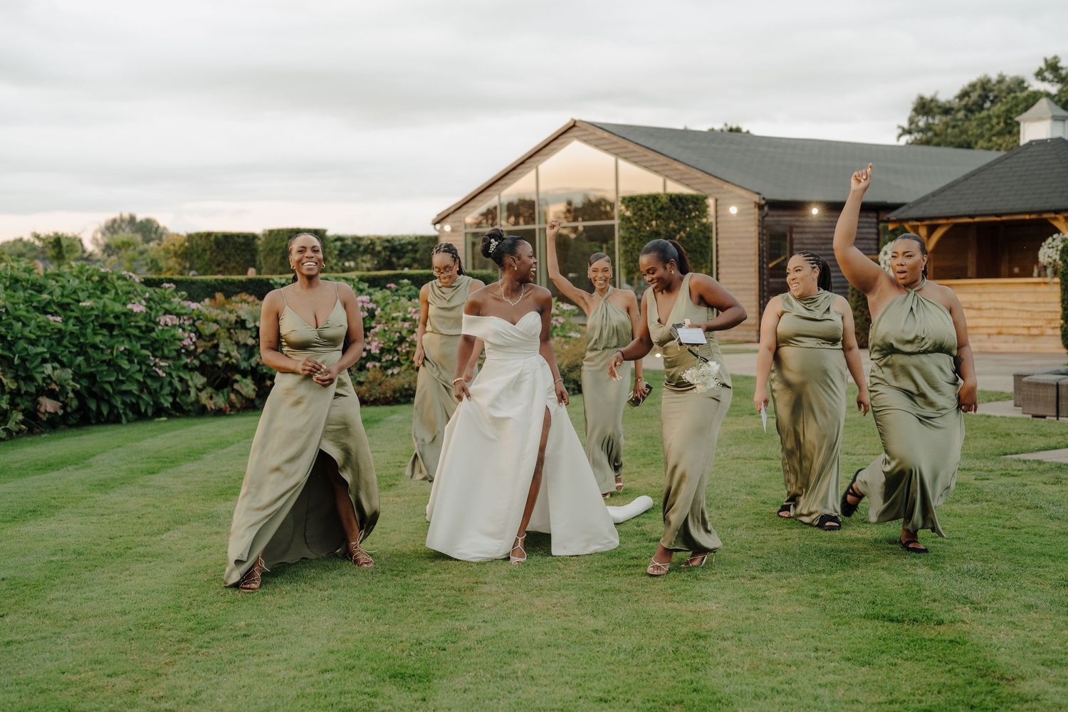 Wedding party members pose playfully on a grassy lawn during outdoor photo session.