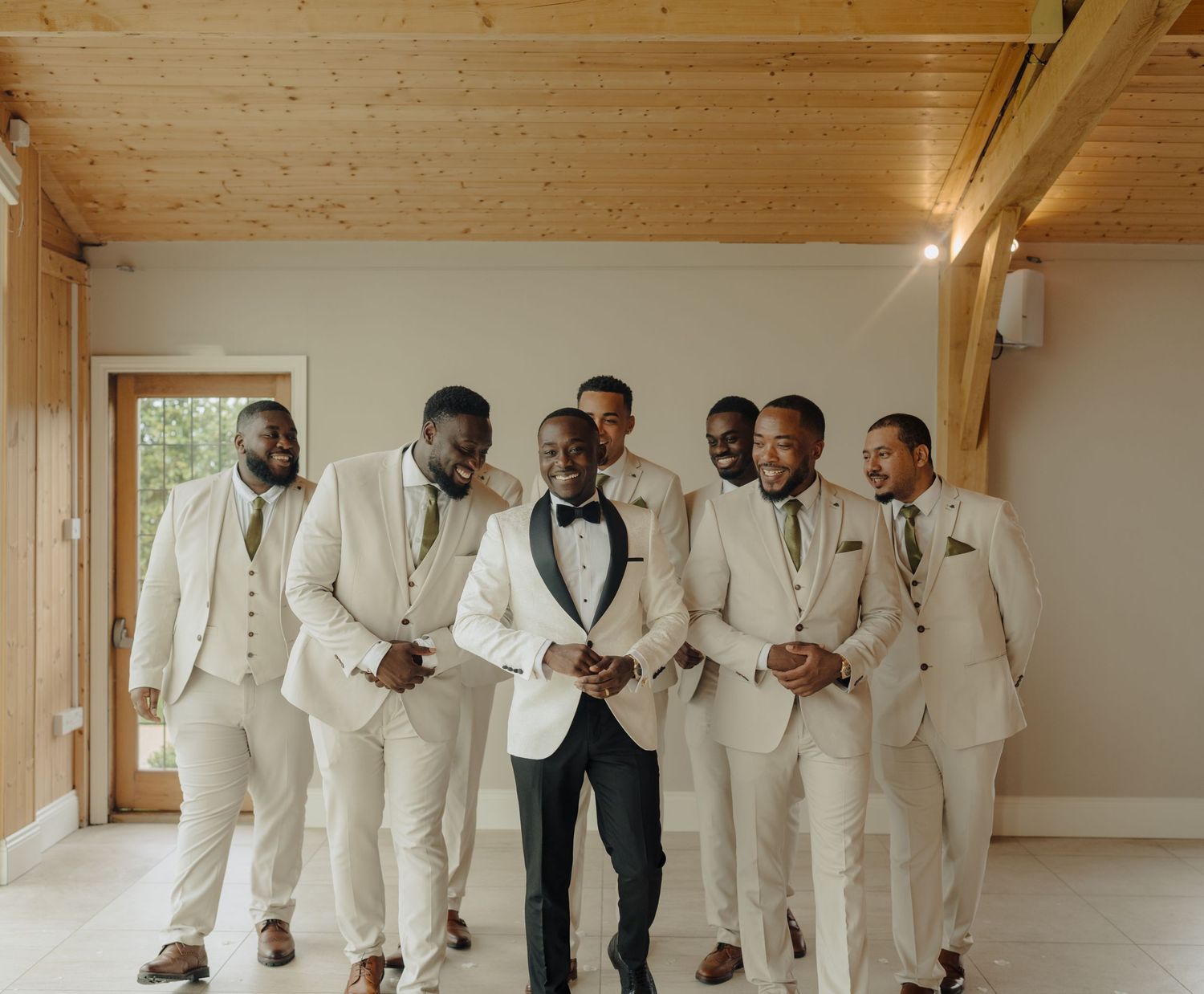 Wedding party members in white suits pose in wooden-paneled hallway.