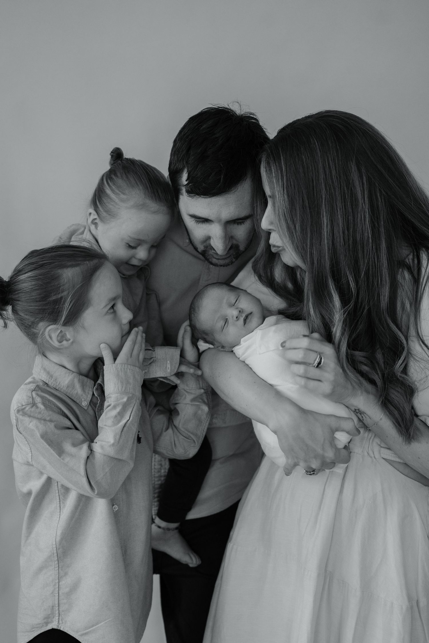Black and white photo sequence capturing tender family moments against a grey backdrop.