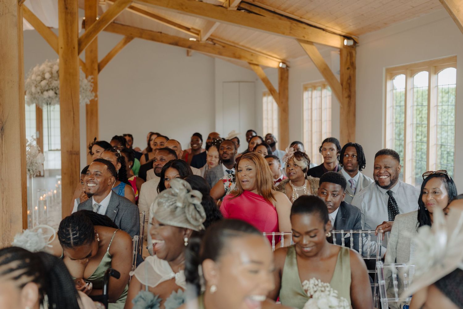 Wedding guests seated in bright venue with natural lighting and wooden architectural features.