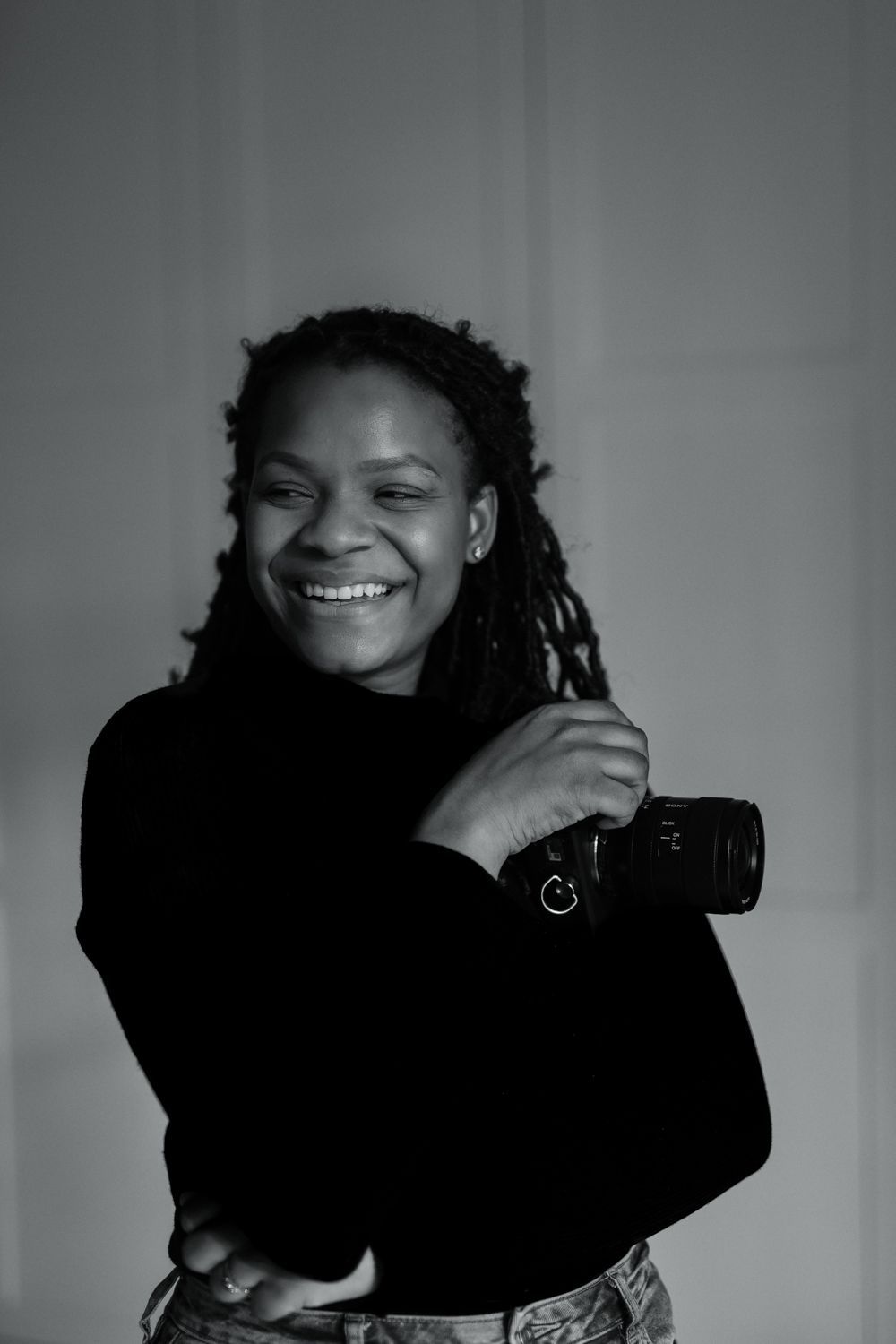 Black and white portrait series showing photographer holding camera and smiling against gray background.