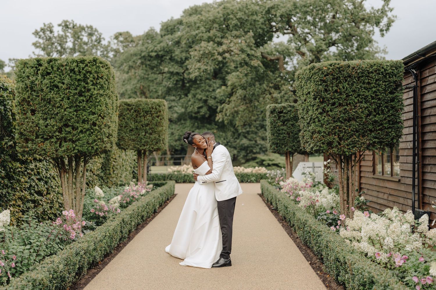 Couple in wedding attire walking through a beautifully landscaped garden path.