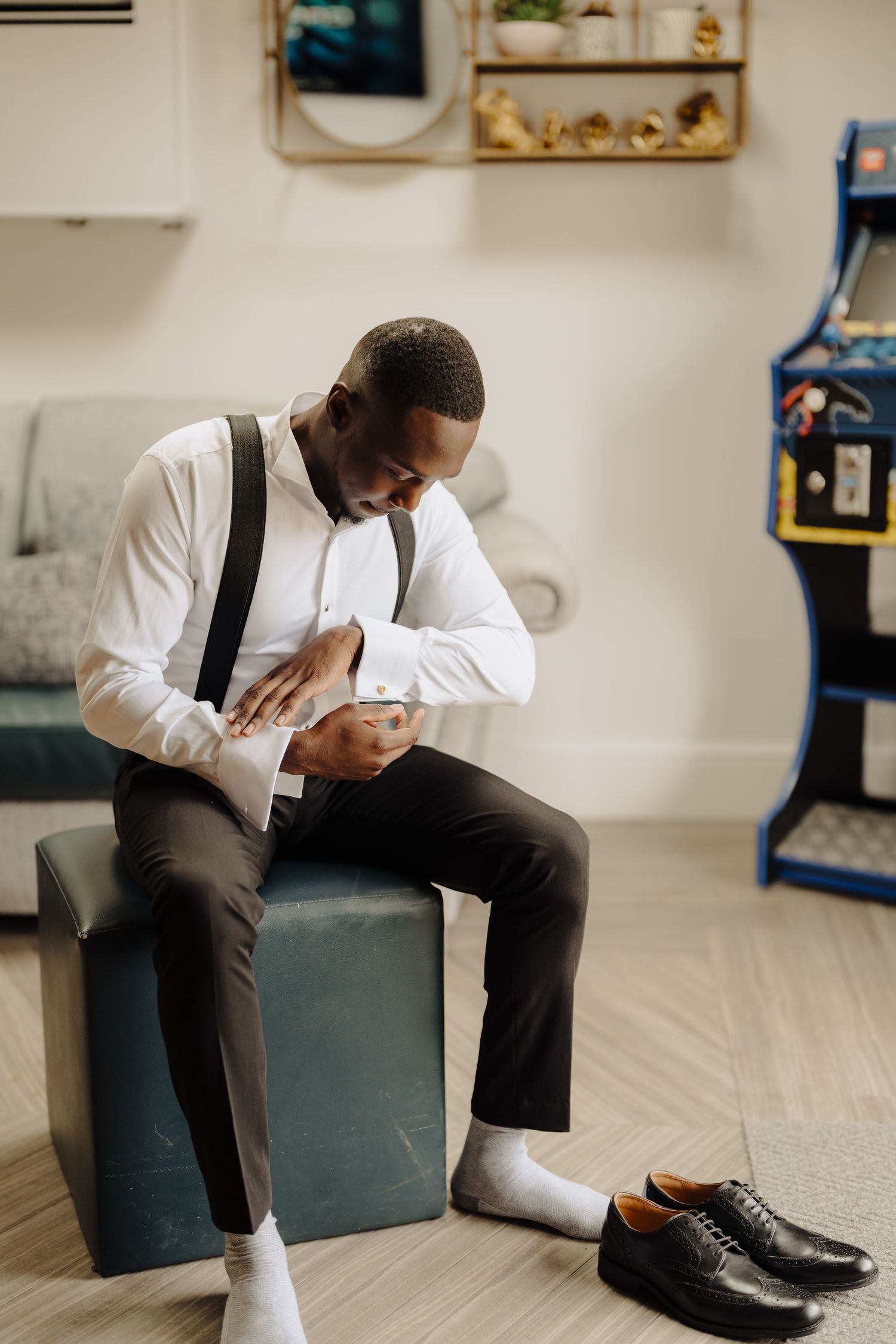 Groom in formal attire sitting thoughtfully on a modern gray ottoman.
