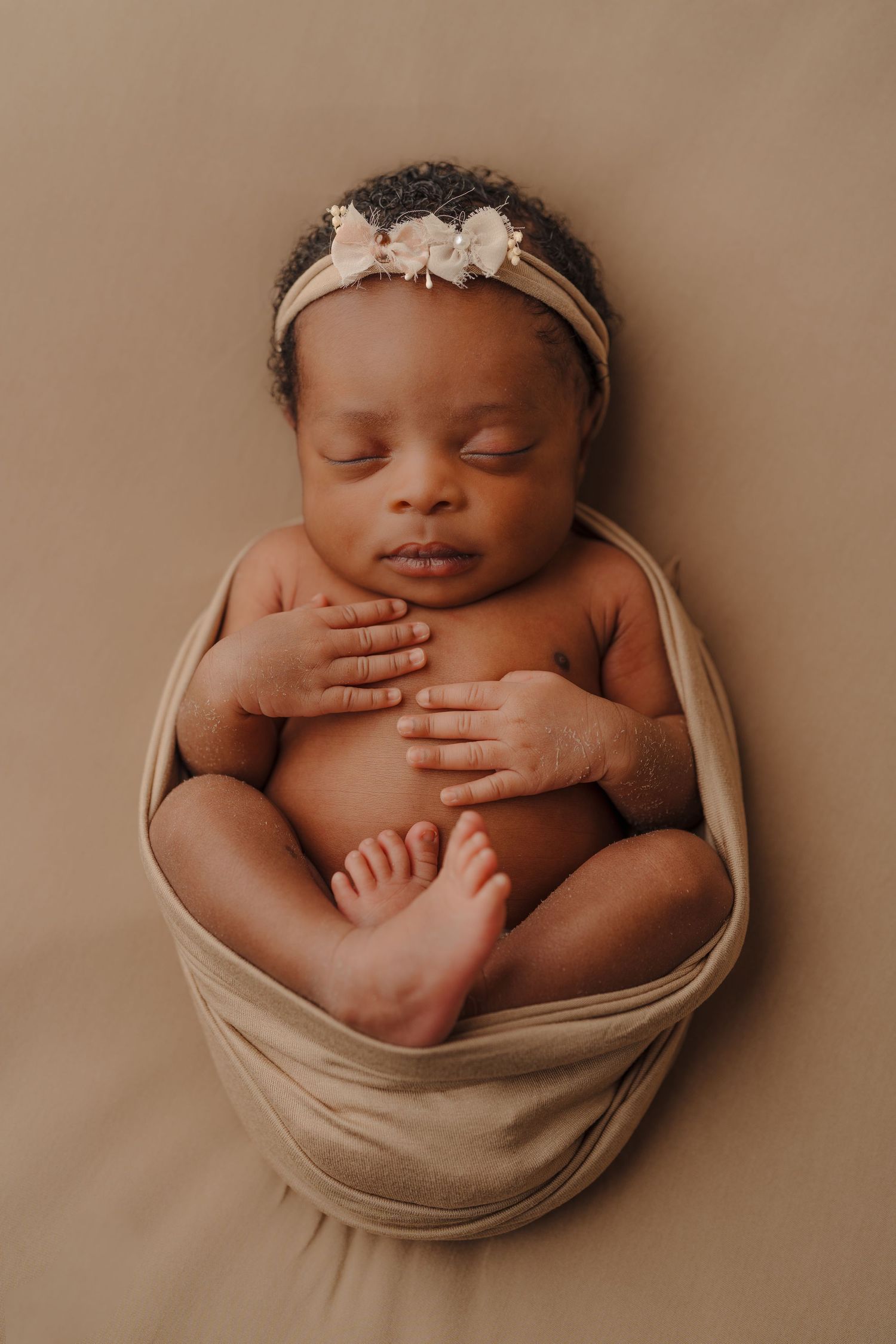 A sleeping newborn posed in a beige wrap with a delicate headband.