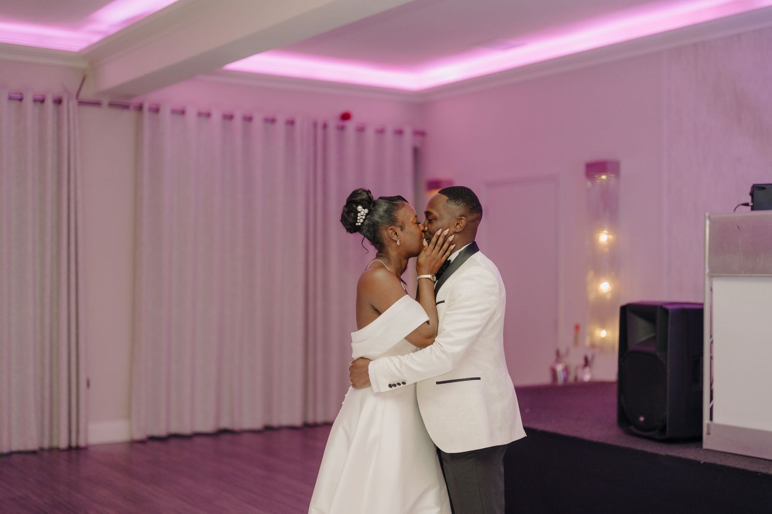 Wedding celebration in modern venue with pink uplighting and white drapes.