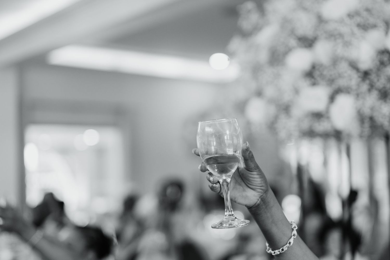 Black and white photograph of wedding guests raising glasses during reception.
