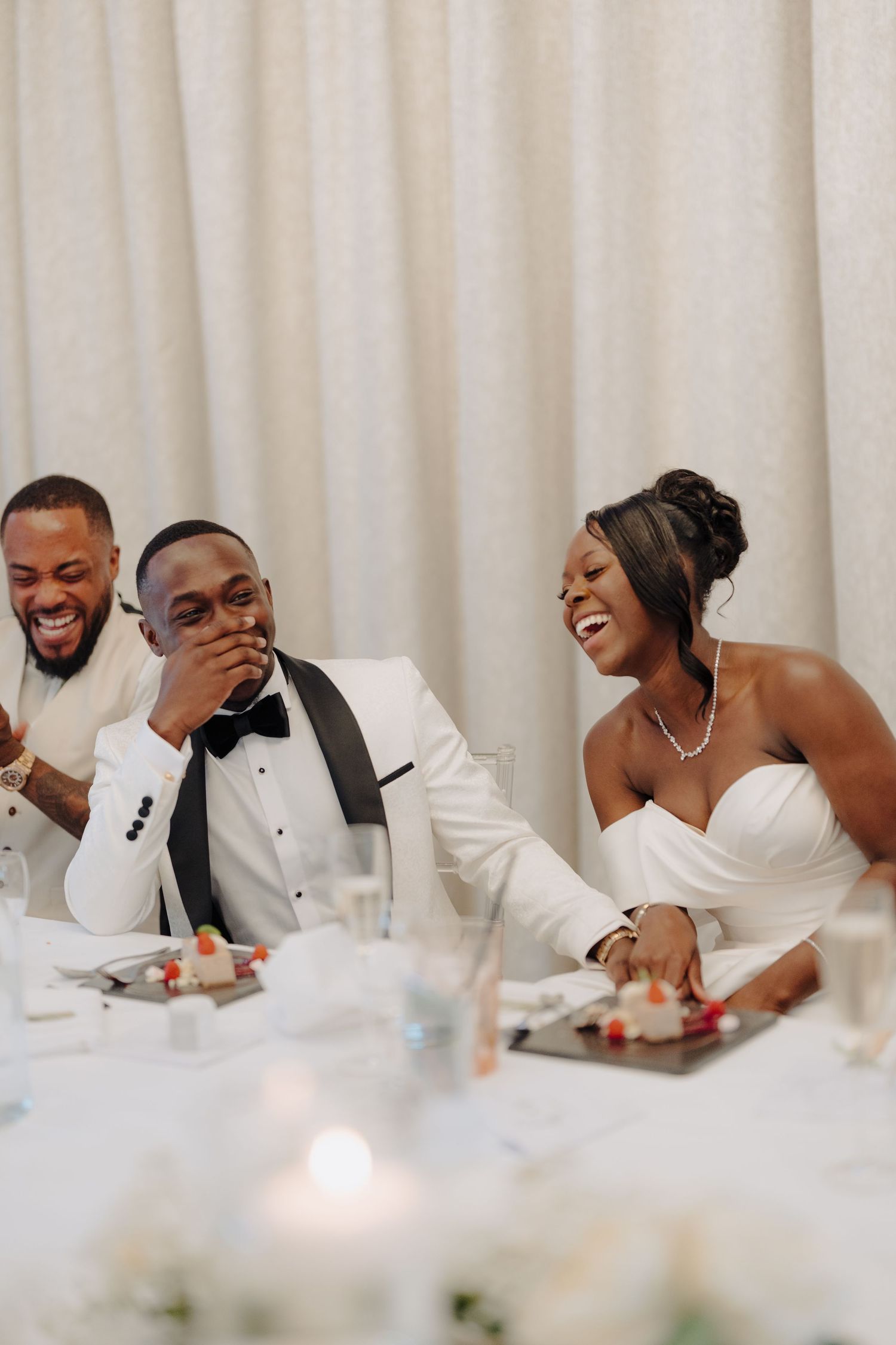 Wedding party laughing together at reception table decorated in white linens.