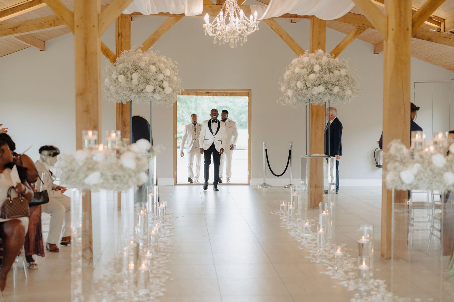 Elegant wedding ceremony setup with crystal chandeliers and white floral arrangements lining the aisle.