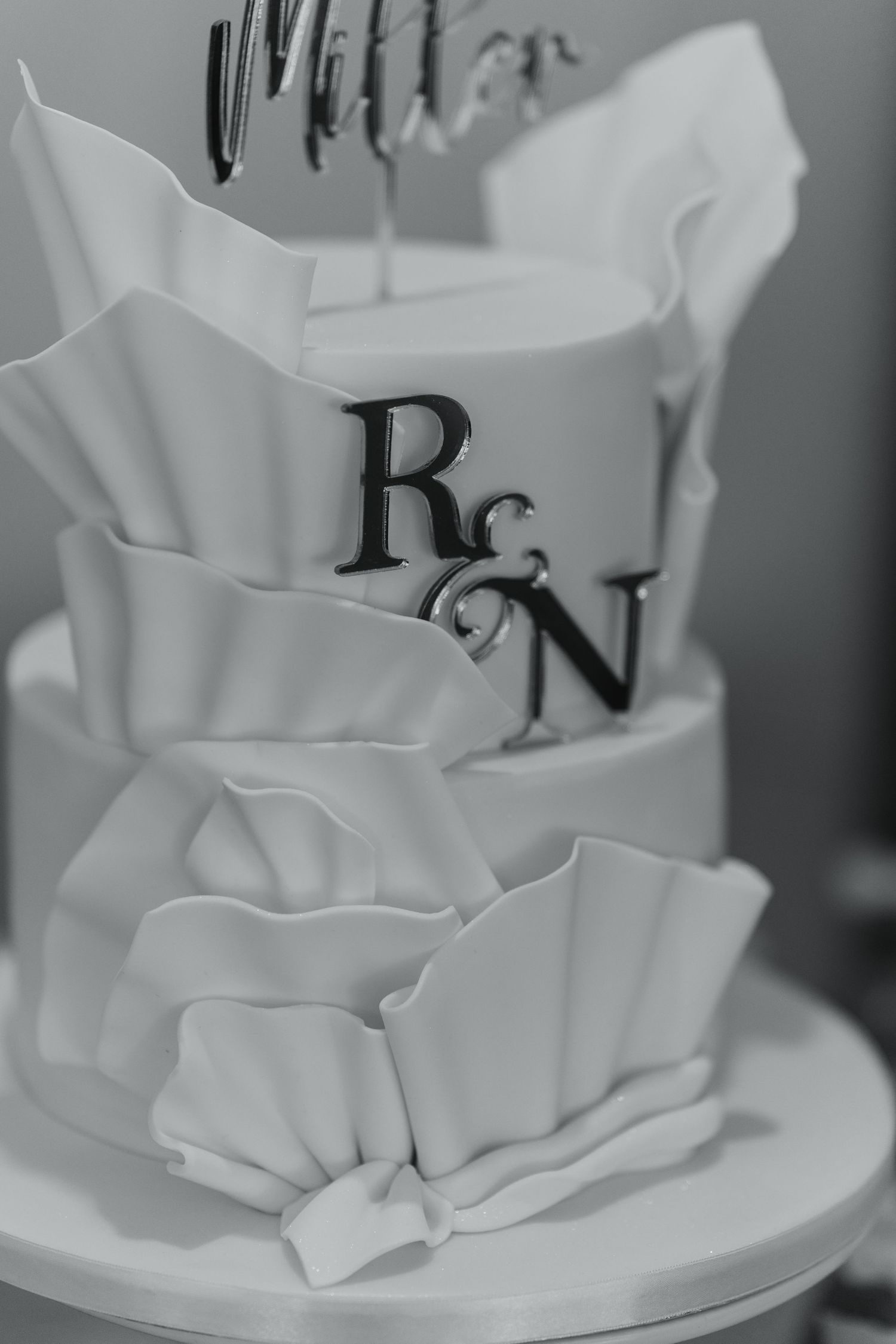 Close-up of a modern white wedding cake with ruffled fondant details.